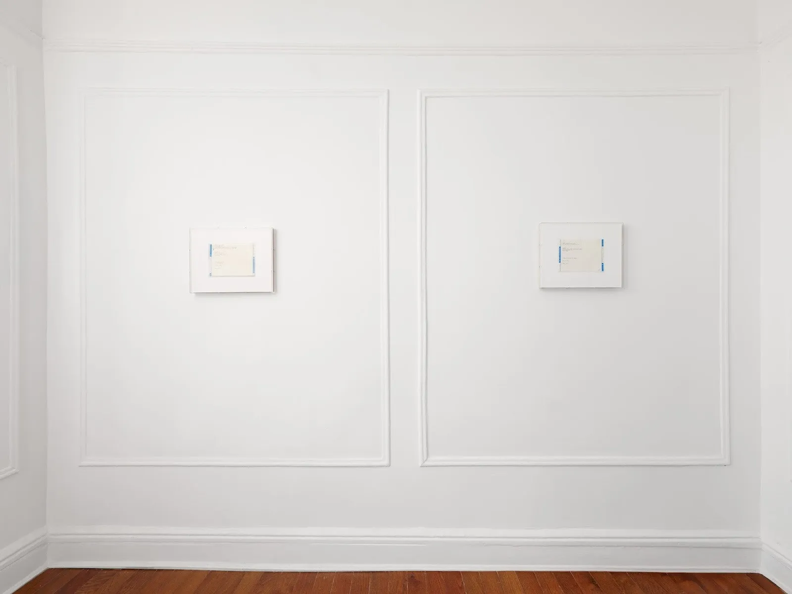 Two framed telegram artworks hang side by side on a white wall with decorative molding in a minimalist gallery space with wooden floors.