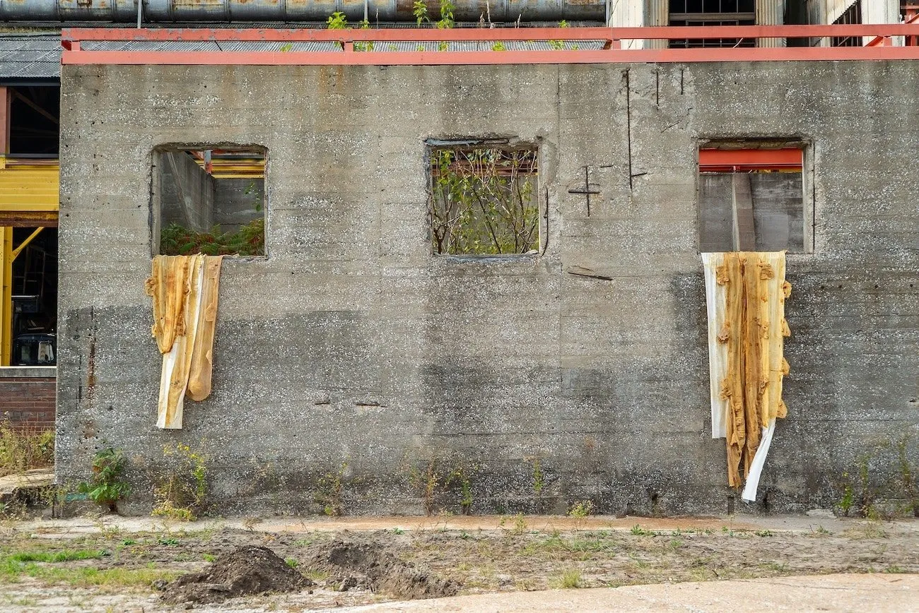 The outside of a dilapidated concrete building features draped brown fabric in two of its three small square windows.