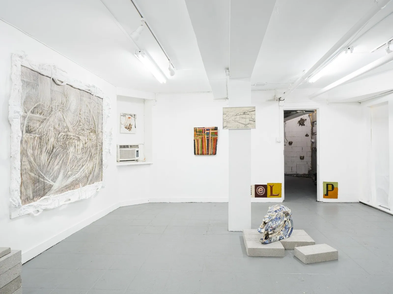 A white gallery space features multiple 2-D and 3-D works of art on its walls, columns, and floor.