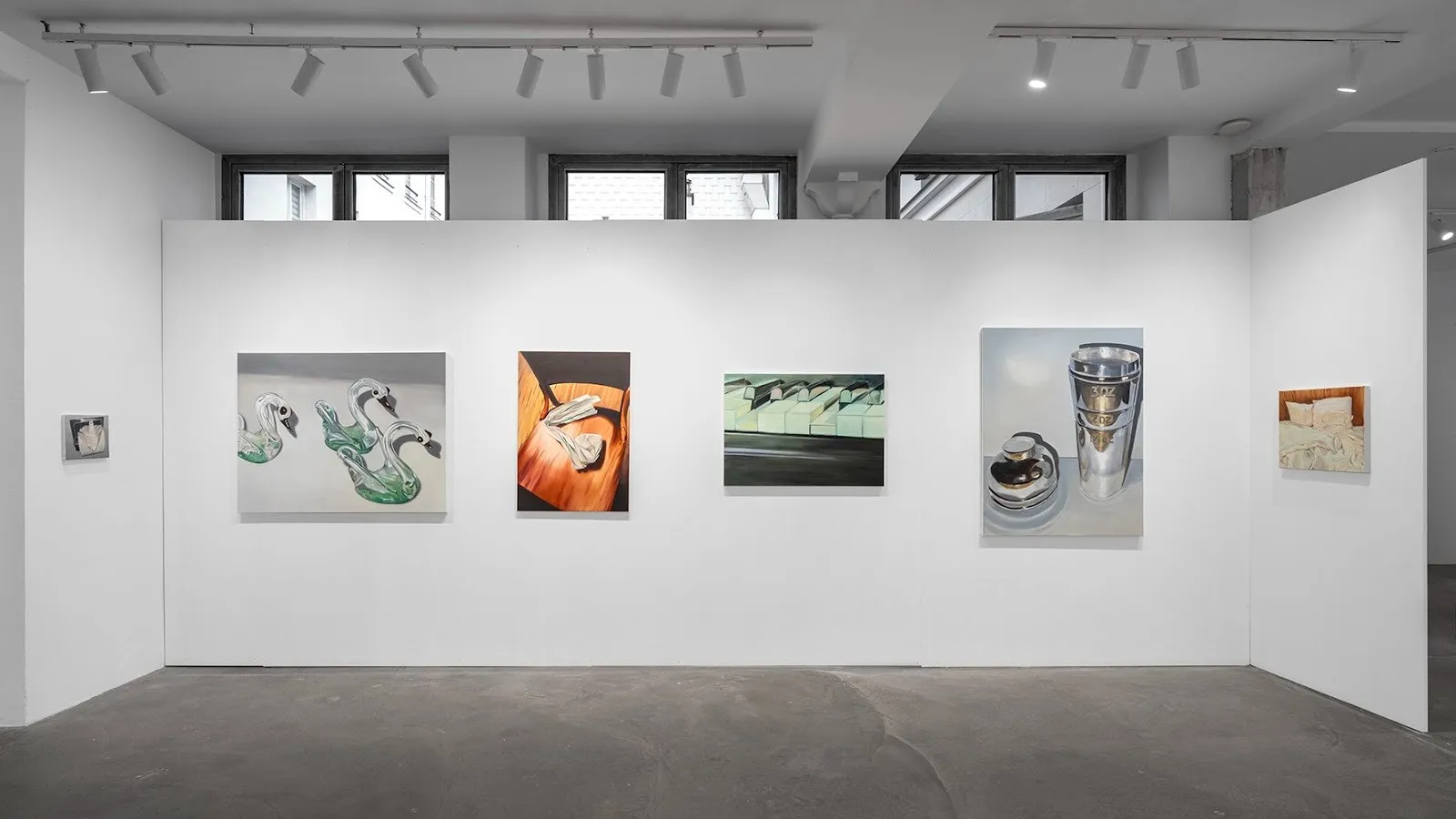 A row of realistic paintings depicting glass swans, folded fabric, and metallic objects on a white gallery wall.