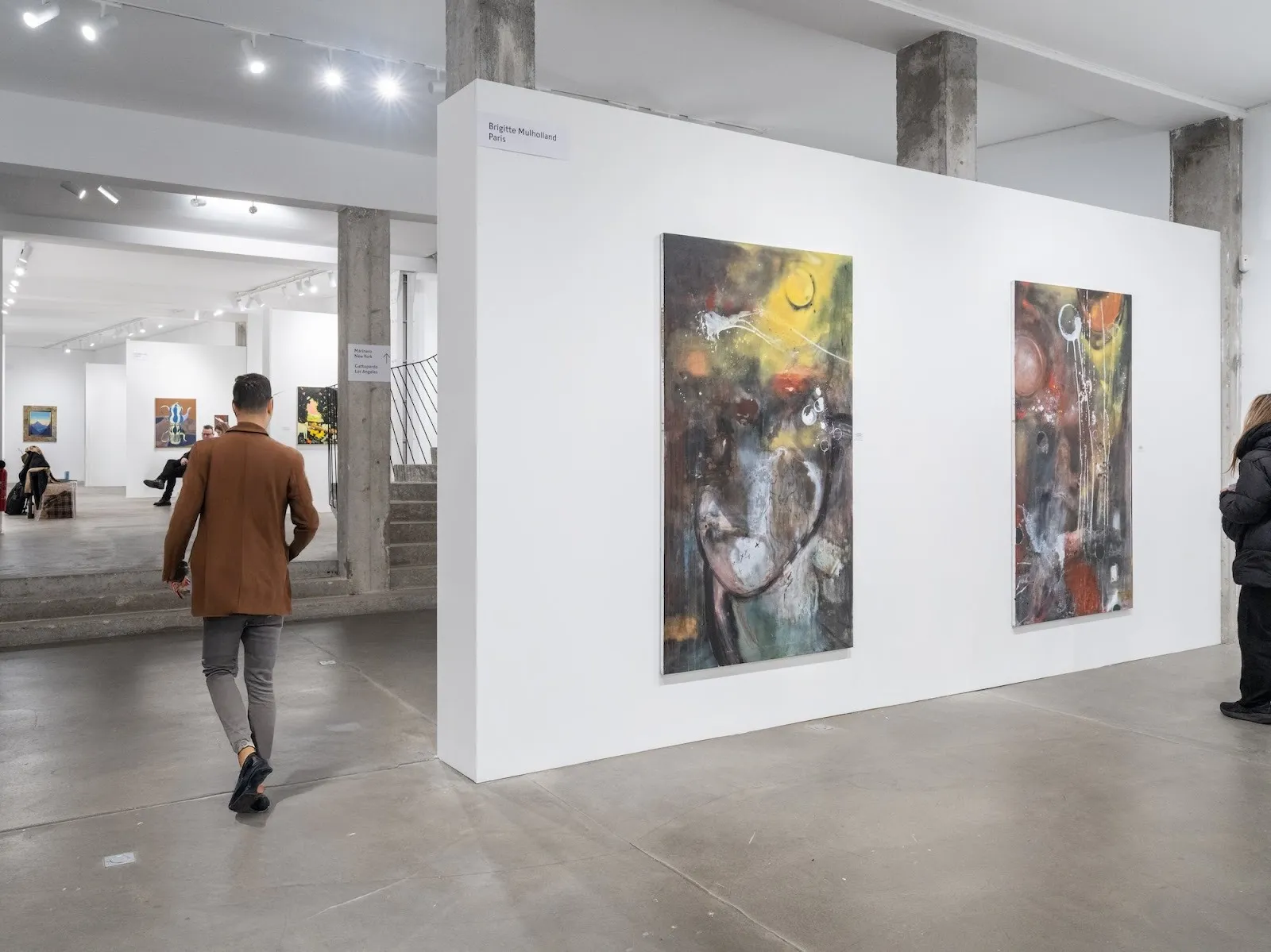 A visitor walking past two expressive abstract paintings in a contemporary gallery space.