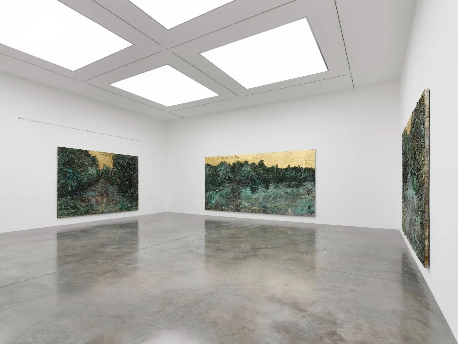In a white gallery room, three similar size and similar composition paintings hang on separate walls. The paintings feature a lush, detailed, green foreground and a golden sky.