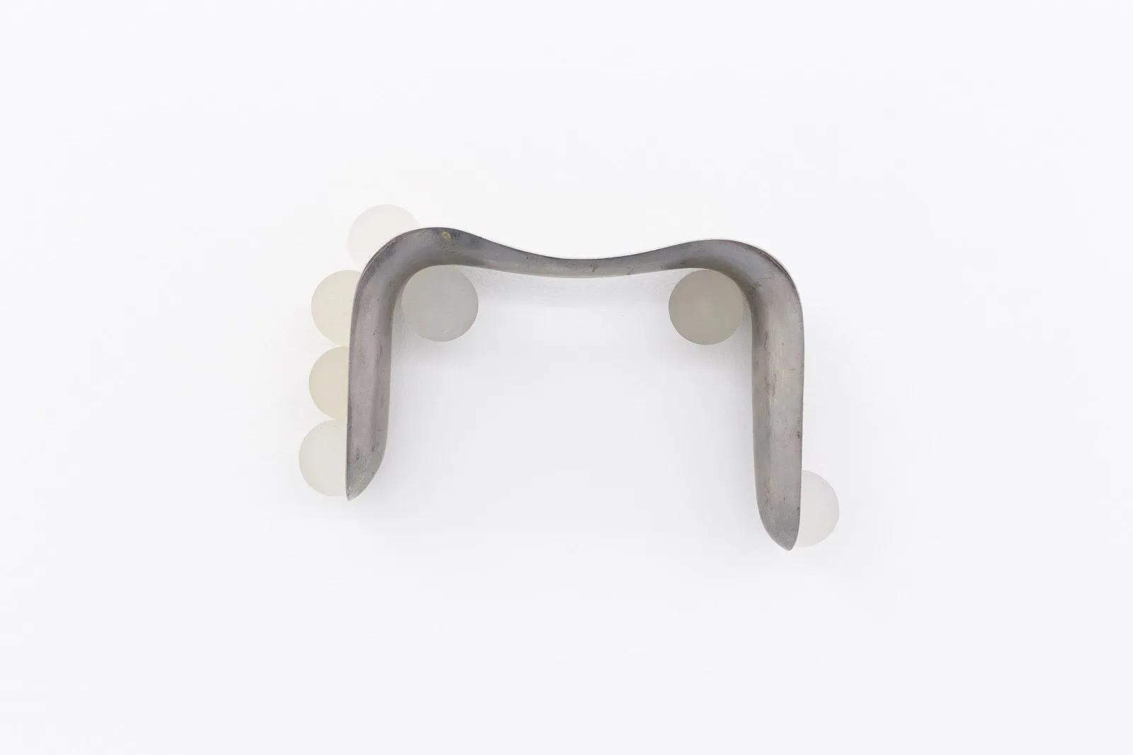 Wall-mounted abstract sculpture made of curved metal with translucent round elements attached.