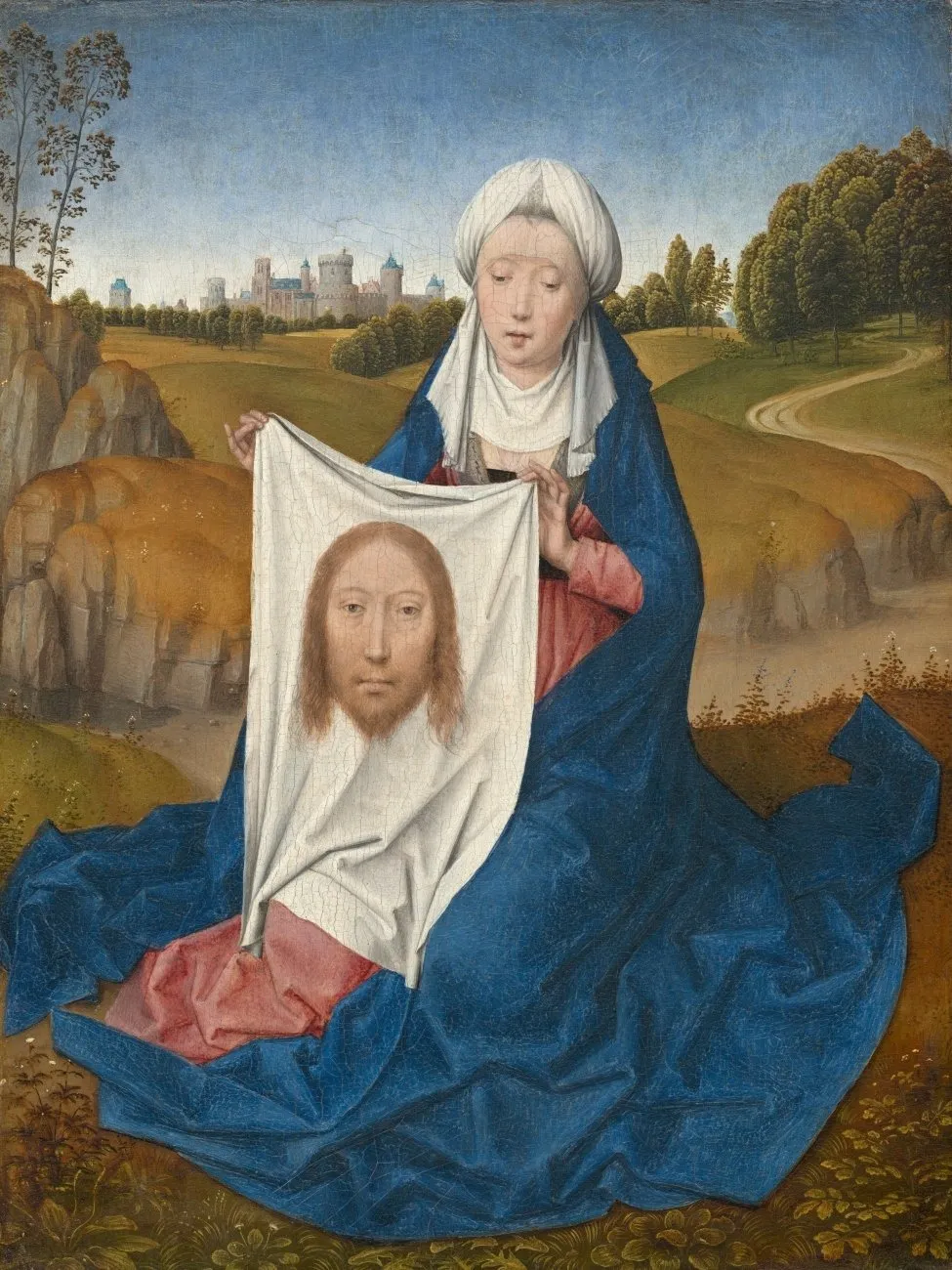 A 15th century oil painting features a woman clad in red and blue robes kneeling in a pastoral setting with a castle in the far distance. The woman holds up a white cloth which has the face of a bearded man (Jesus).