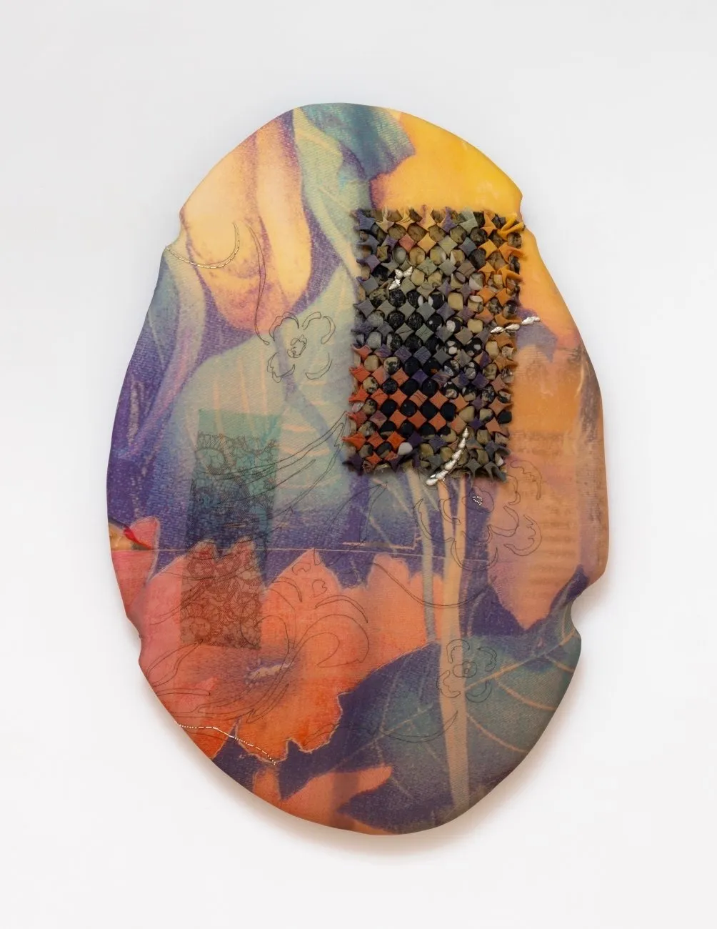 An oval panel with small dents on the side is overlaid with colorfully designed and dyed fabric. The fabric features oranges, greens, and blues in abstracted flower designs. In the top right, an intricately folded patch of fabric forms a grid.