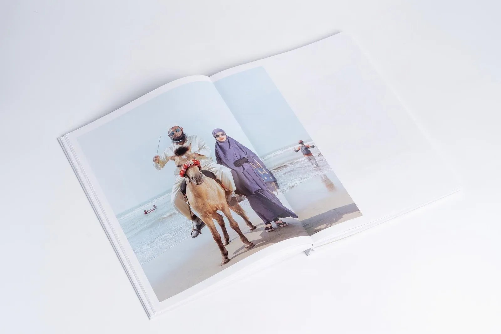 A book lying open features a photograph that stretches from the left page to part of the right. The photograph depicts a man riding a horse, posing next to a woman in sunglasses and red lipstick.