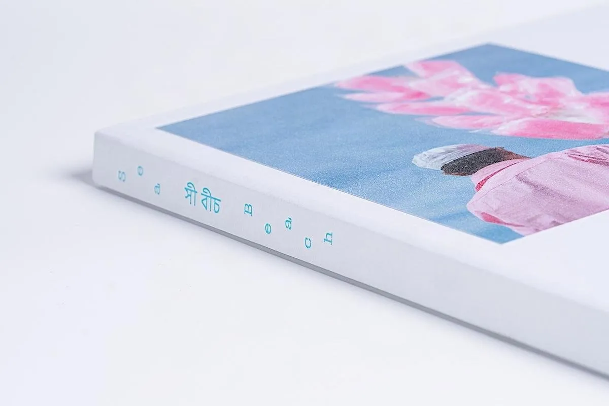 A book lying on its side is mainly white with a photograph in the left corner. The spine of the book features the words "sea beach" in blue.