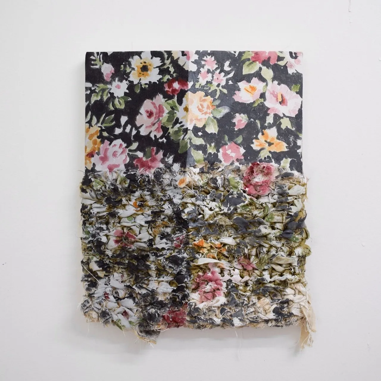 A textile-based artwork with floral patterned fabric partly unraveled, layered with rough, woven textures in muted dark tones.