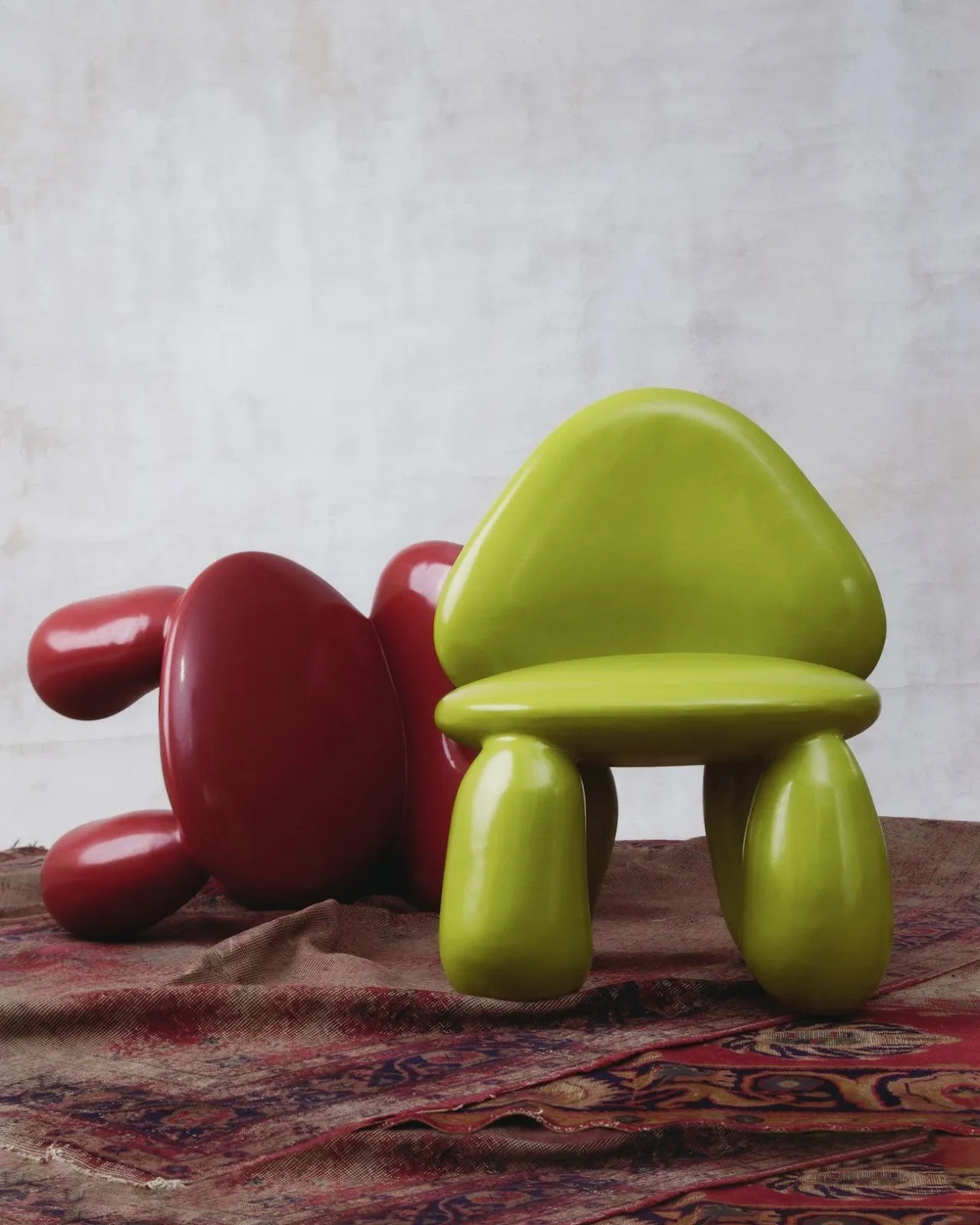 Two glossy, playful chairs shaped like cartoonish figures—one in bright lime green, upright, and one in deep red, lying on its side.