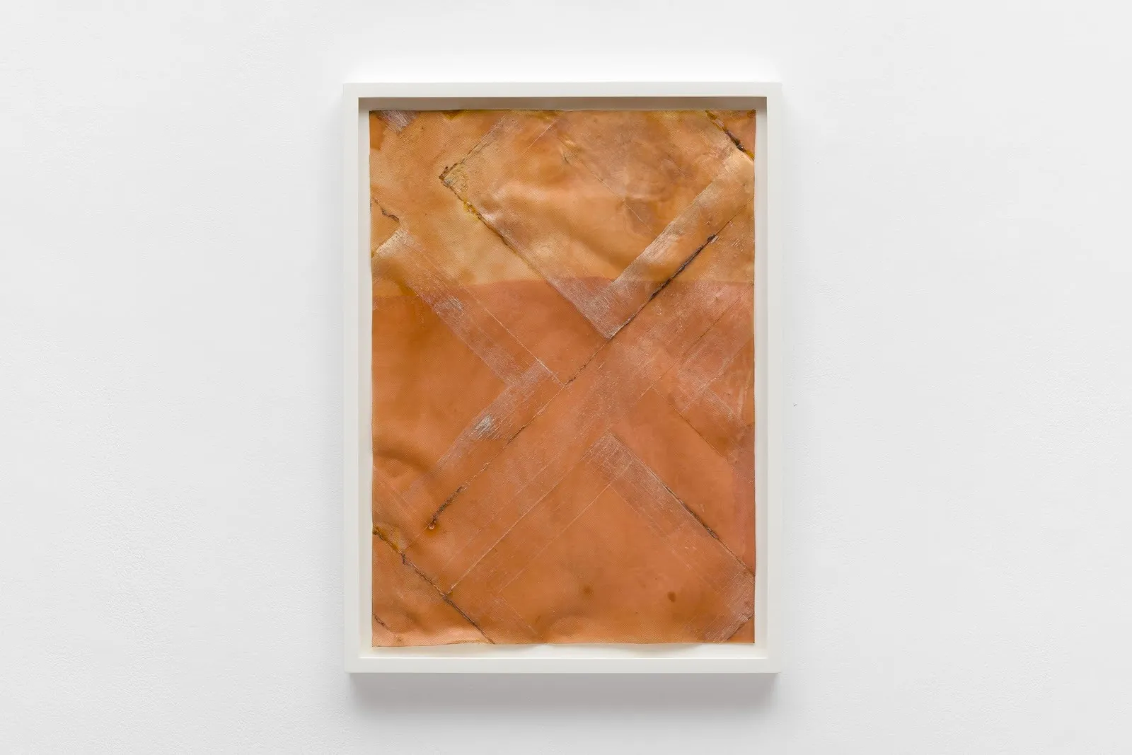 A white-framed wall work is mostly flat, made of brown, almost fleshy, overlapping latex. The surface features patterned square impressions, some with dark lines and white impressions.