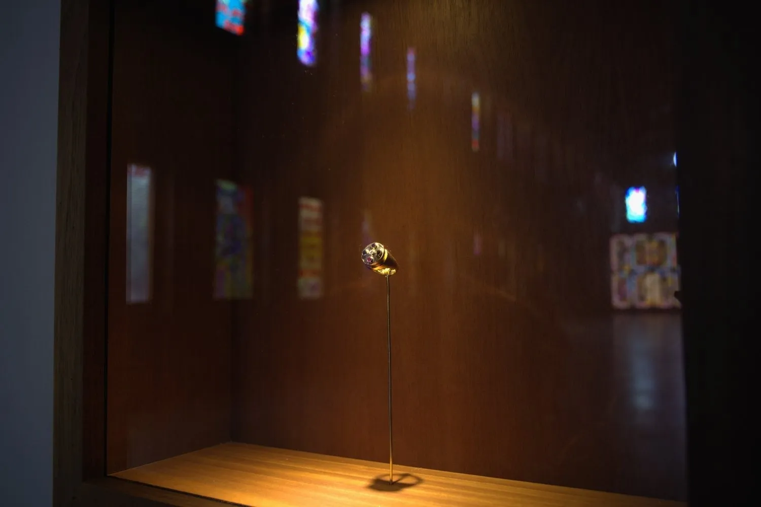 A ring, spotlight by golden light and affixed to a thin stand, is golden and has five gemstones set into the face.