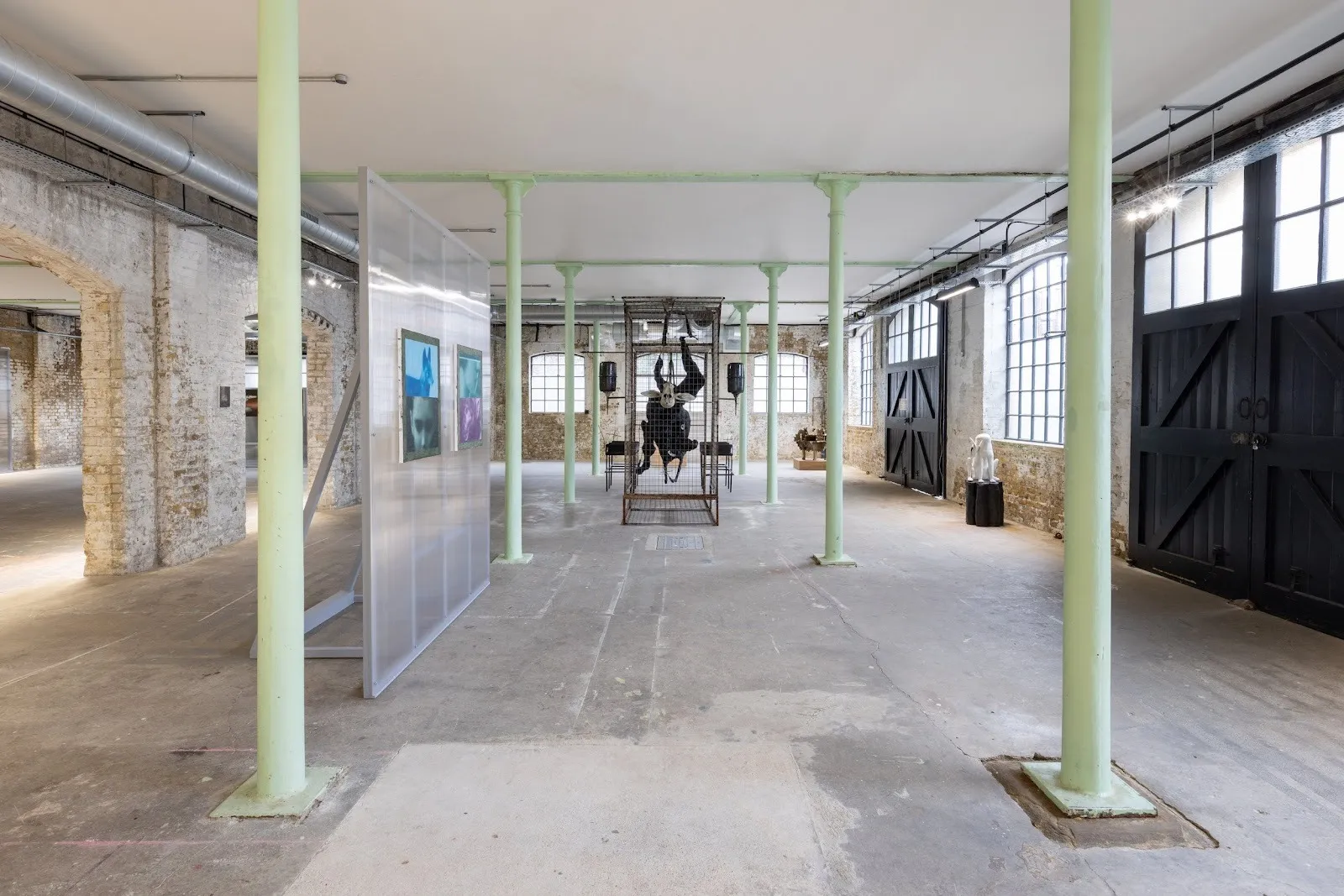 A large, cement and stone warehouse with green supporting columns is populated with various sculptures and wall works.