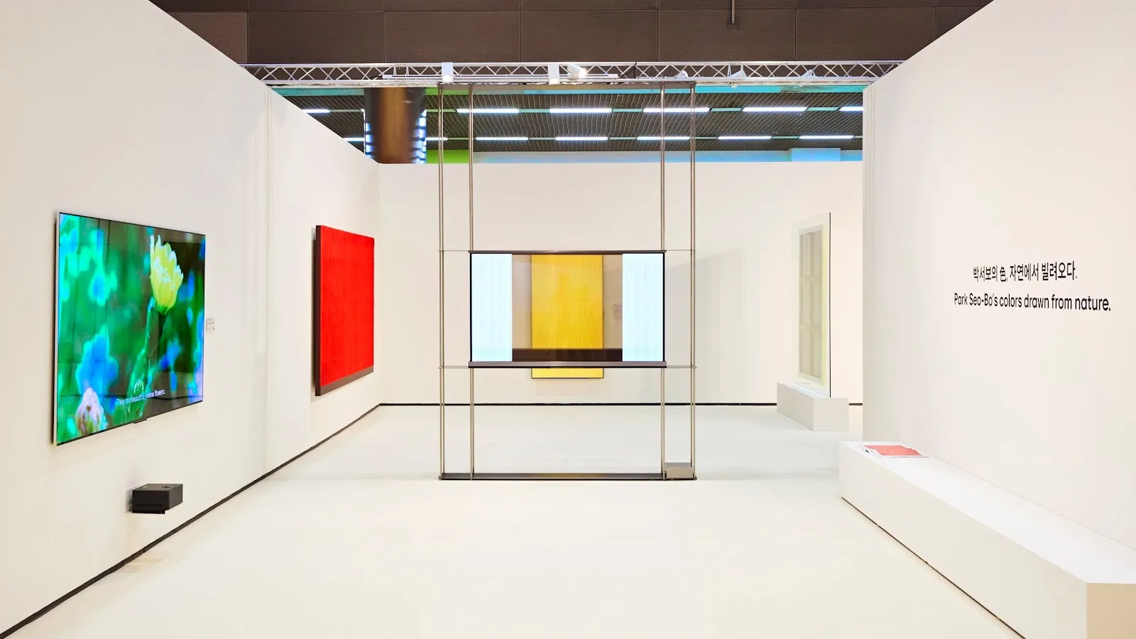 A white gallery booth features a variety of brightly colored wall and video works.