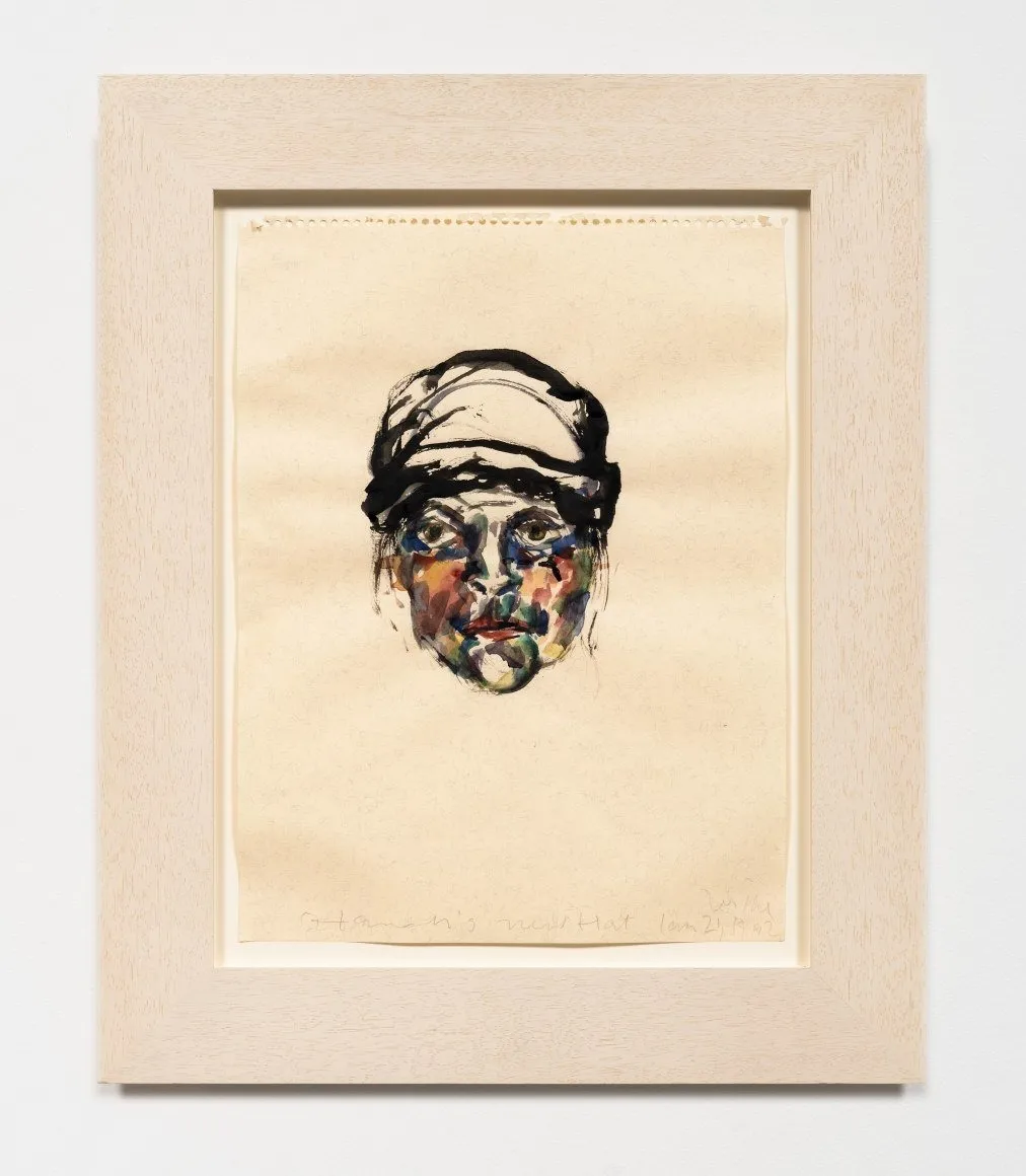 A thick, wood-framed watercolor on beige paper features a slightly abstracted face made from washes and strokes of blue, red, yellow, and black paint.