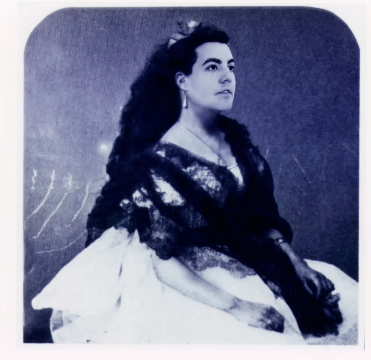 Vintage, black and white photograph of a person with long hair in a full, lacy dress gazing up and off to the right.
