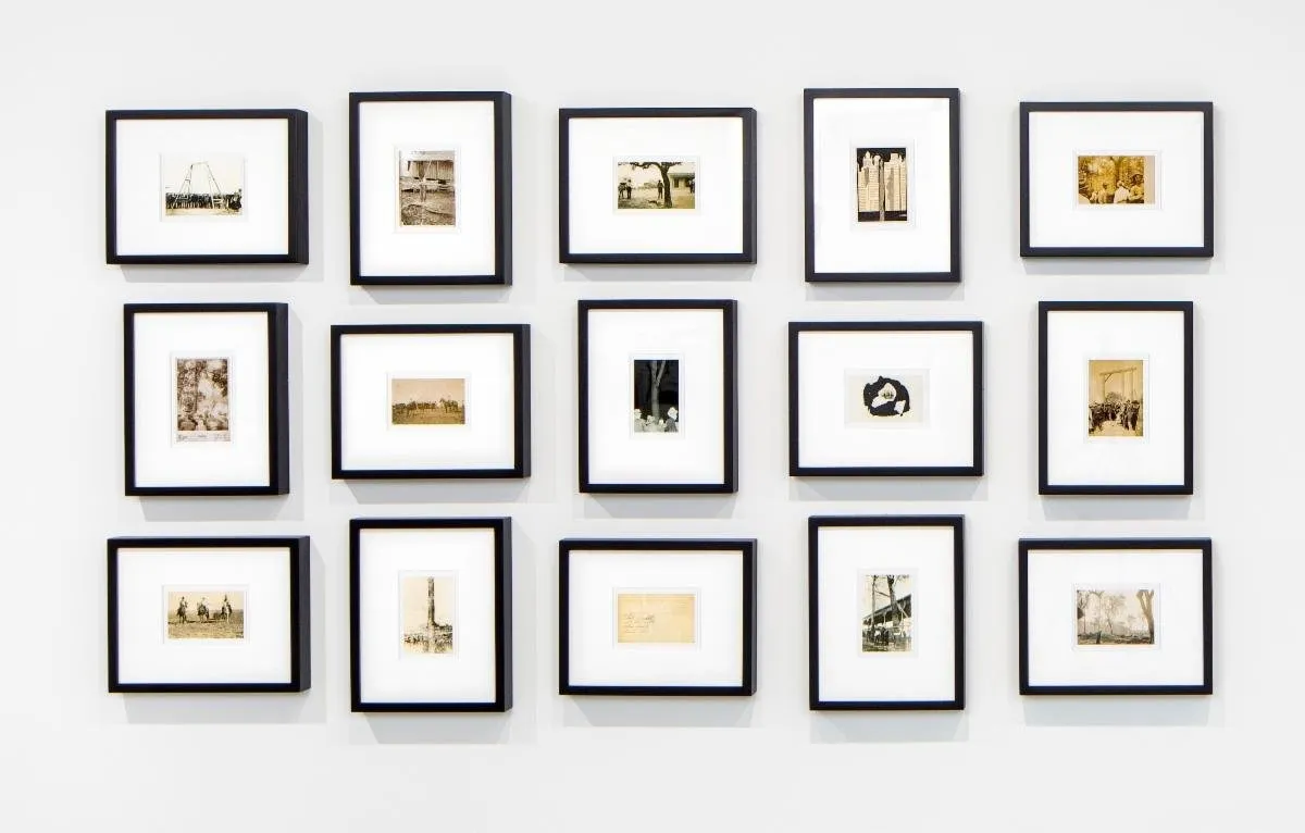 A wall displays a grid of fifteen framed photographs of varying dimensions but similar, smaller size. Each image depicts a different image; all seem to be in black and white or sepia.