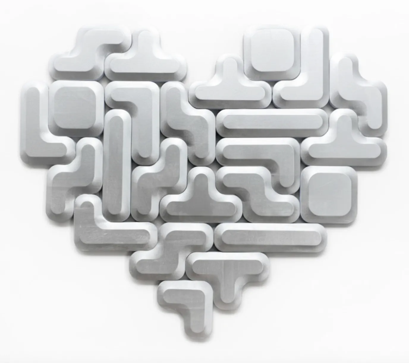 Metallic silver modular shapes assembled into a heart formation on a white wall.