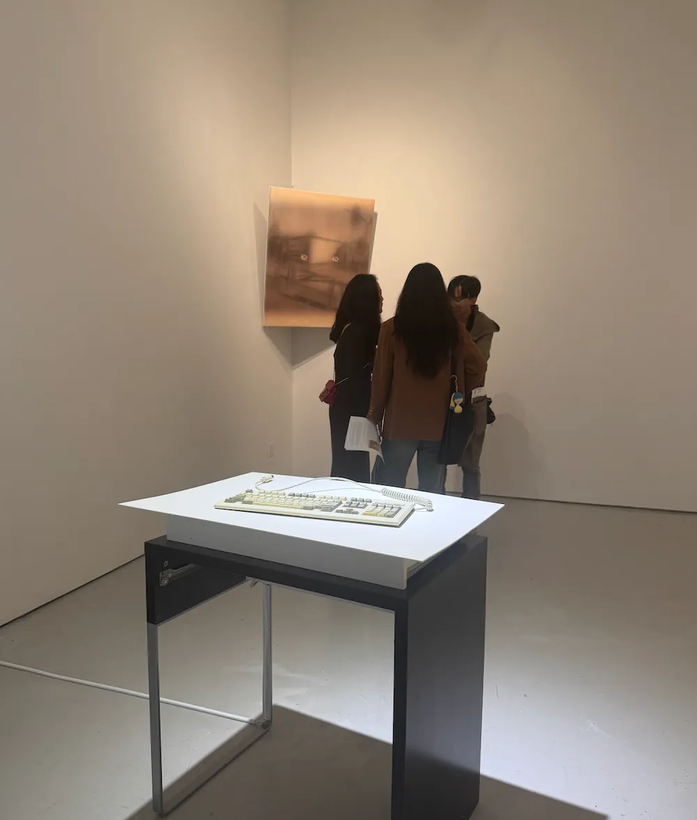 Three people viewing a sepia-toned painting in a gallery, with a sculptural keyboard on a table in the foreground.
