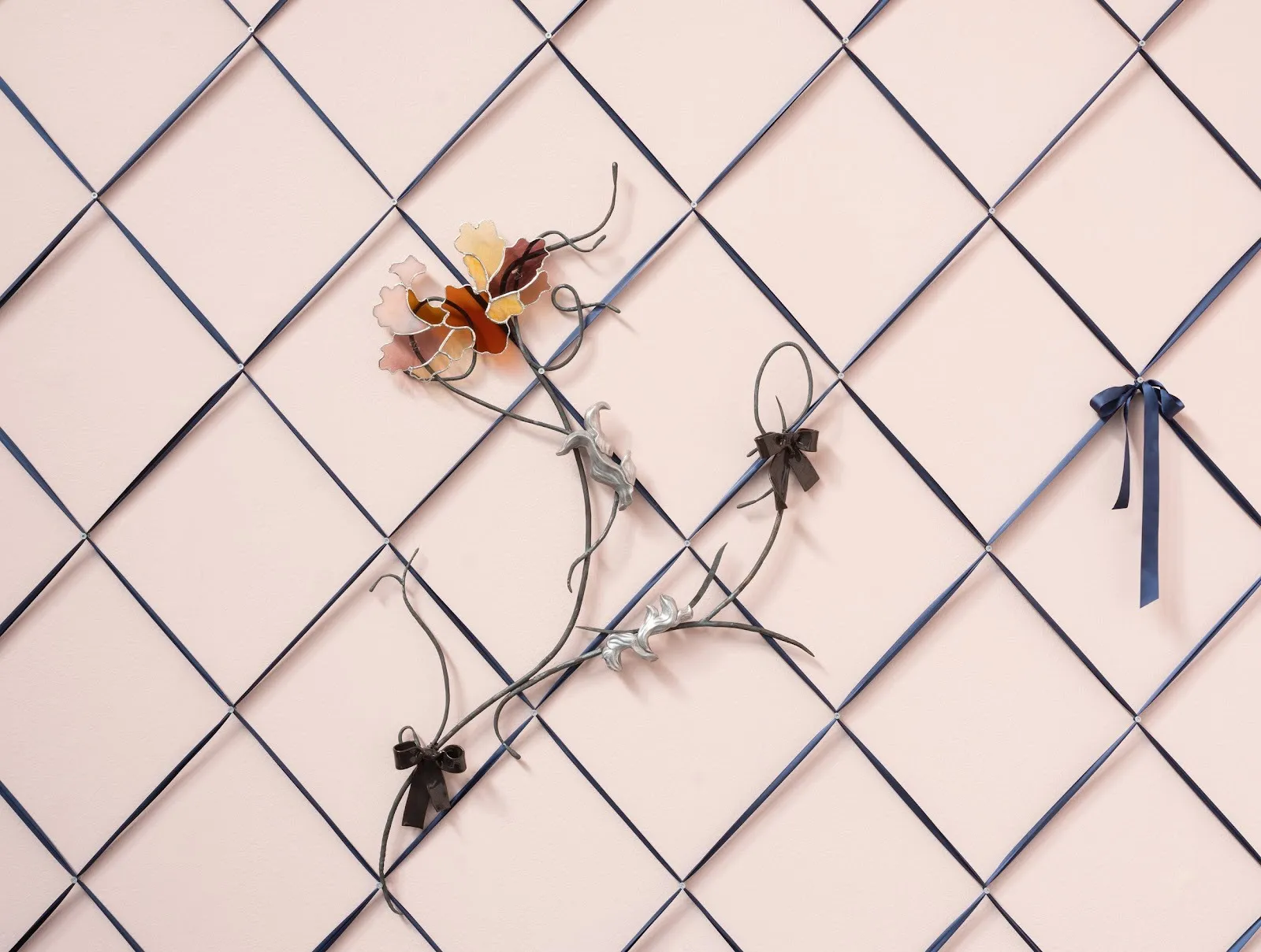 Ribbon is laced in diamond lattices across a pink wall, secured by small pearls at each cross. Threaded into the ribbon are delicate glass flowers and ribbon bows.