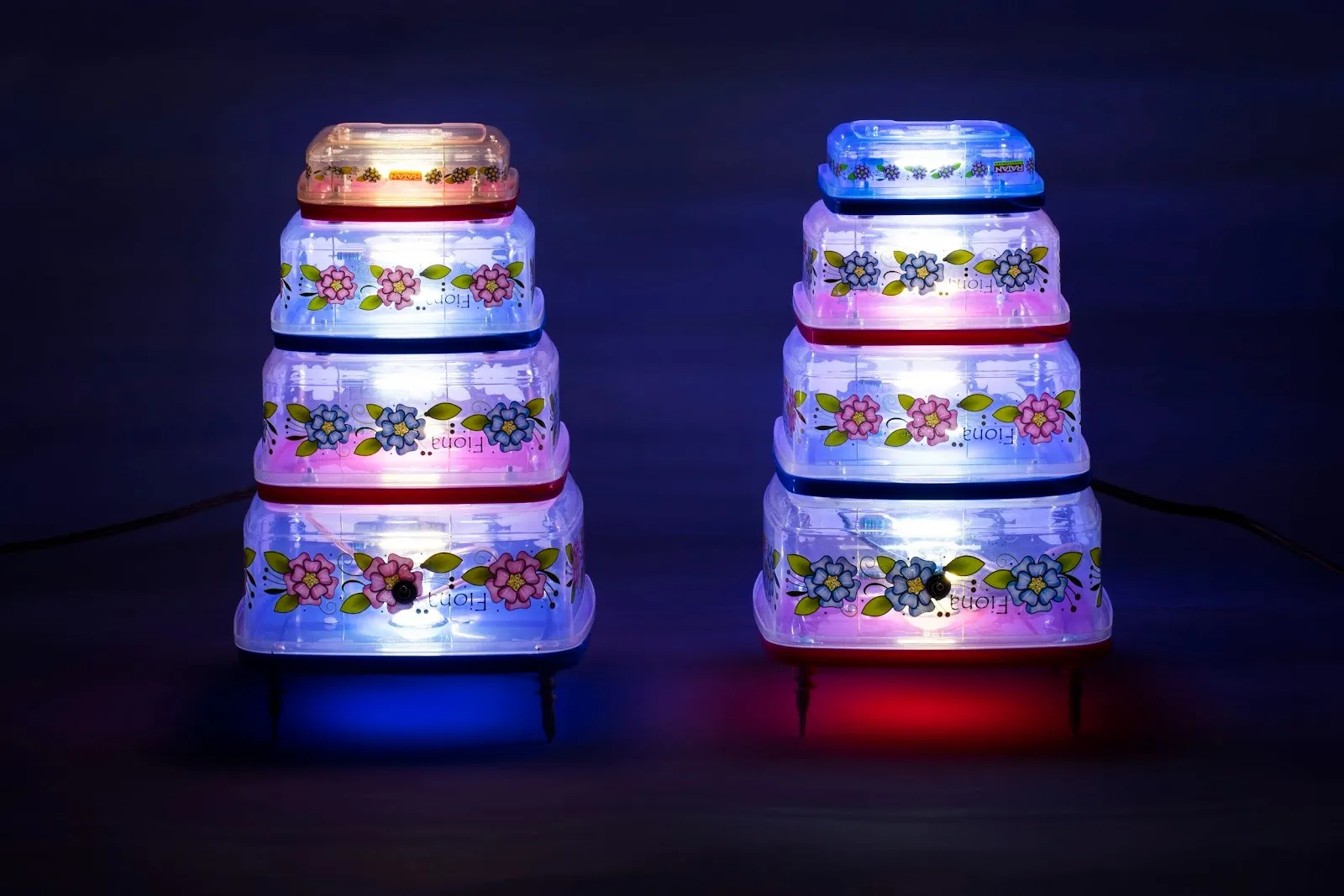 Two lamps feature similar designs: four-tiered, transparent shaeps with floral decorations. The tiers decrease in size to the top. The light is cast red and blue from the colors of the tier dividers.