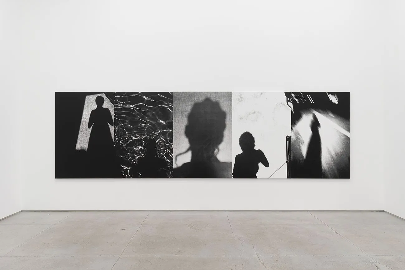 Black-and-white panel of shadowy silhouettes arranged in five sections on a gallery wall.
