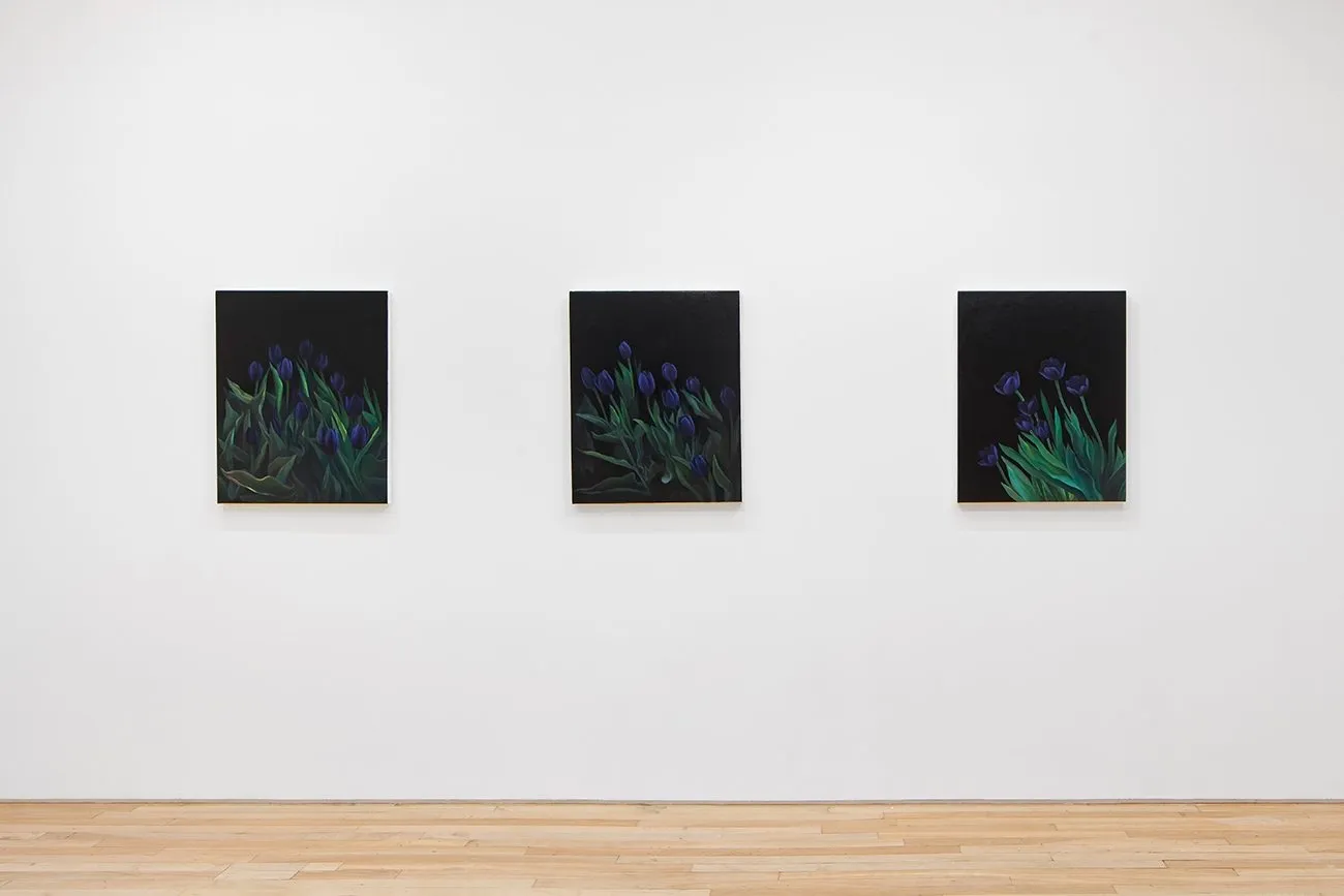 Three canvases of dark tulips with green leaves against black, hung on a gallery wall.