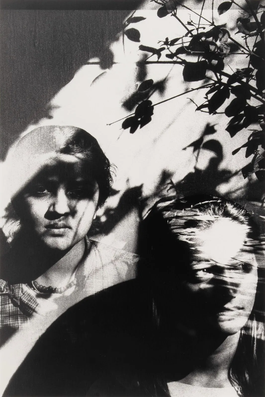 Black-and-white photograph of two overlapping faces partially obscured by leaf shadows and double exposure effects.
