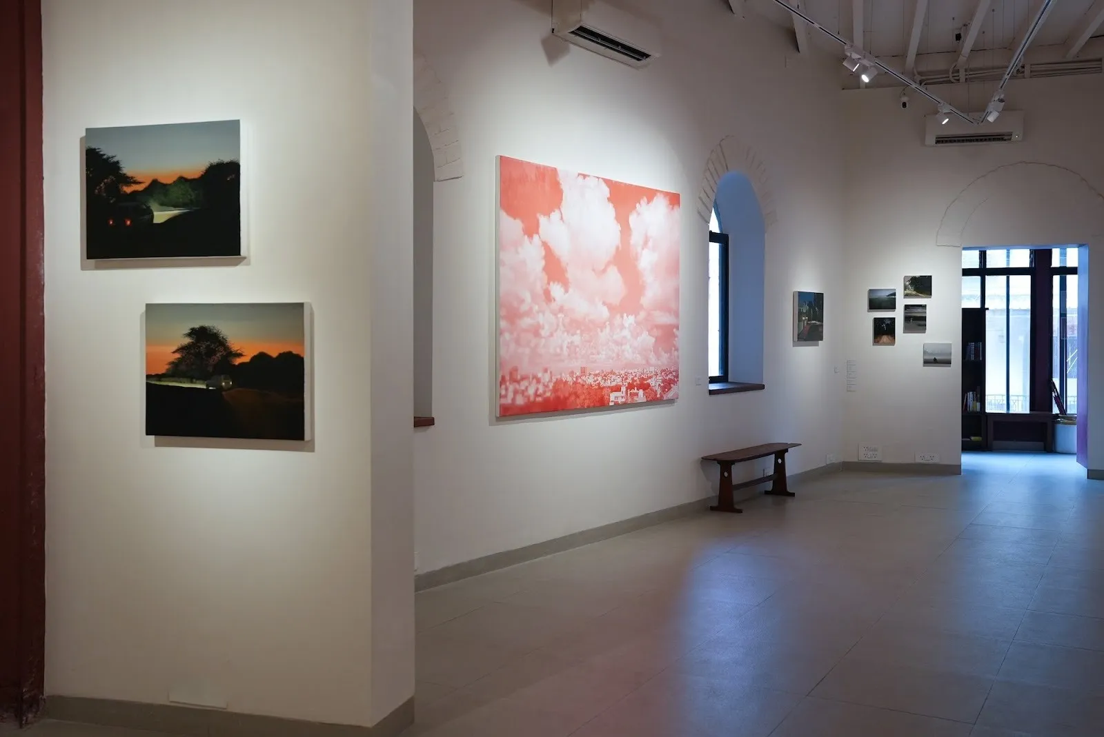 Gallery installation view showing paintings hung along white walls in a vaulted exhibition space with arched windows.