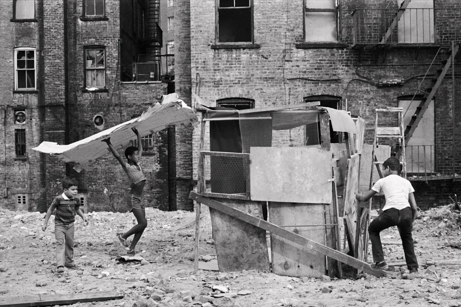 Children build and climb a wooden structure in a rubble-filled vacant lot.
