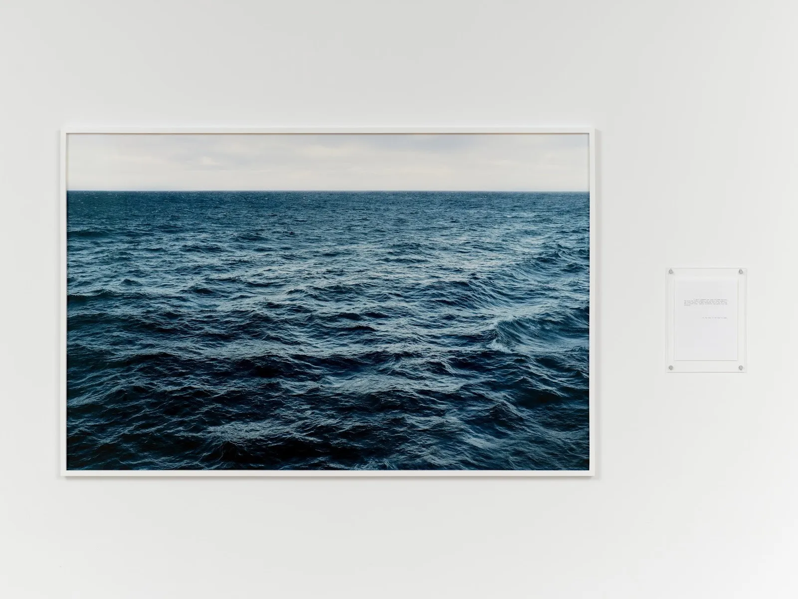 Large framed photograph of a dark, rippling ocean horizon mounted on a white gallery wall.
