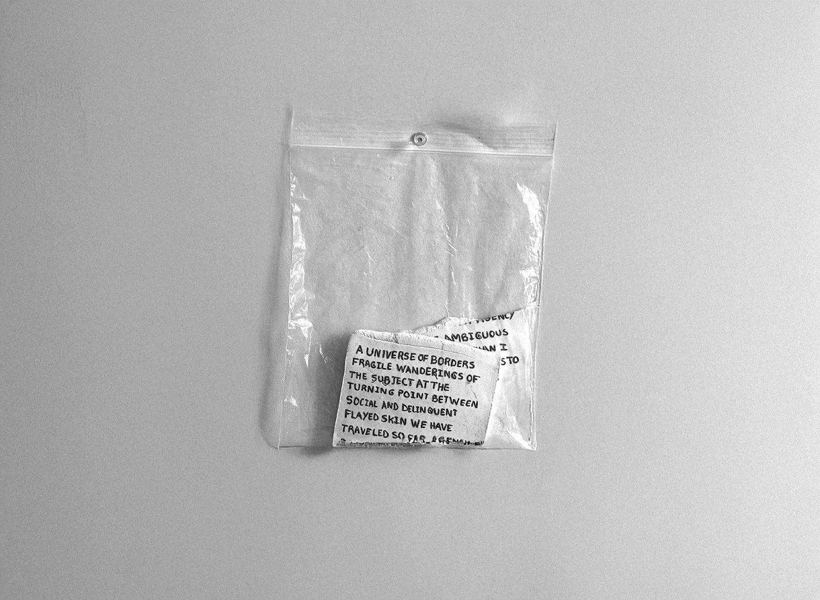 Small handwritten text fragments folded and sealed inside a clear plastic zip bag pinned to a wall.