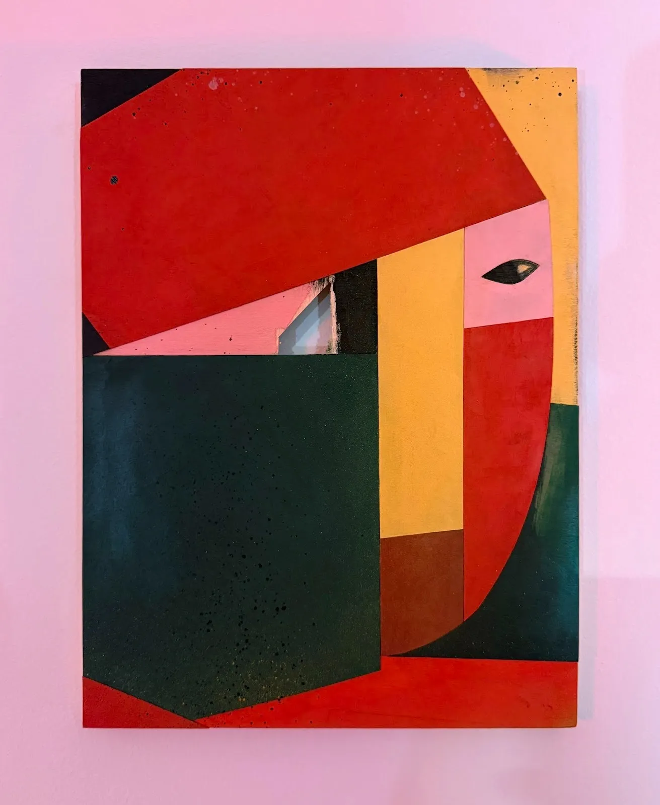 Abstract geometric painting composed of red, green, yellow, and black planes, featuring a small eye-like form embedded in the composition.