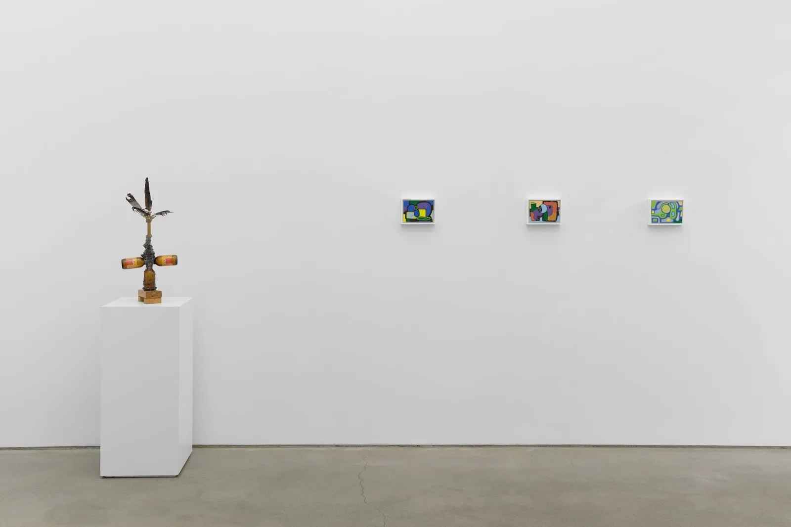 Minimal gallery wall with a small sculptural object on a pedestal and three colorful abstract paintings hung in a row.
