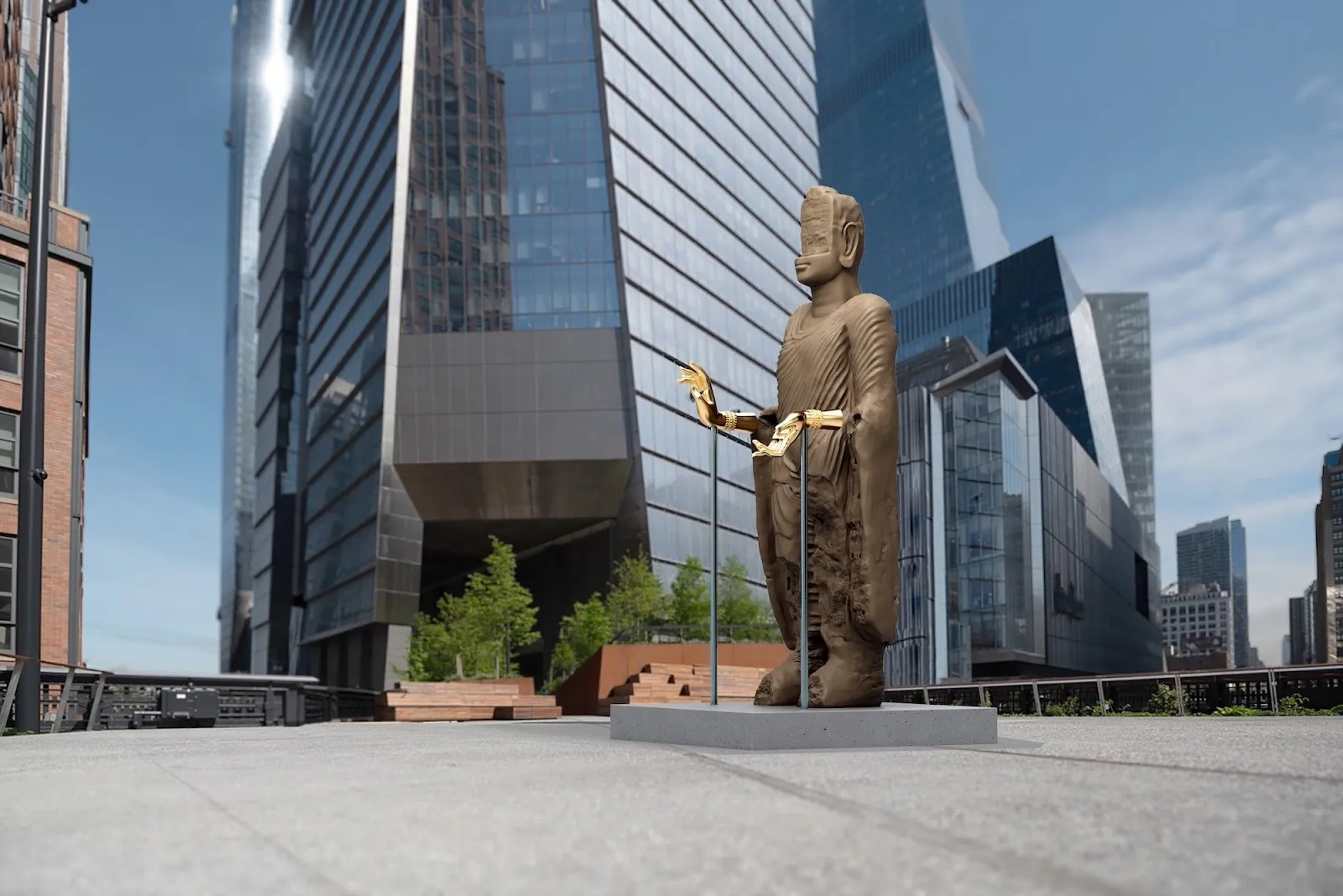 Side view of a large Buddha figure with gold hands, set against contemporary architecture along the High Line.