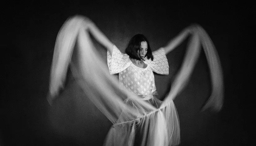 Woman in a flowing dress captured in motion, fabric sweeping outward in a dramatic black-and-white photograph.
