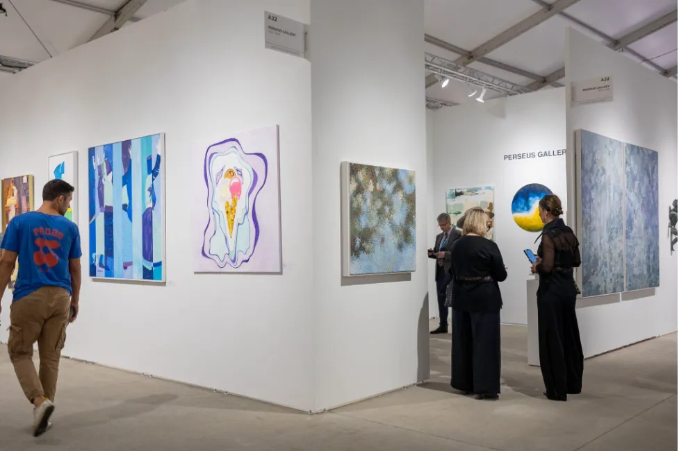 An interior view of an art fair booth presented by Perseus Gallery, featuring various contemporary abstract paintings and visitors browsing the displays.