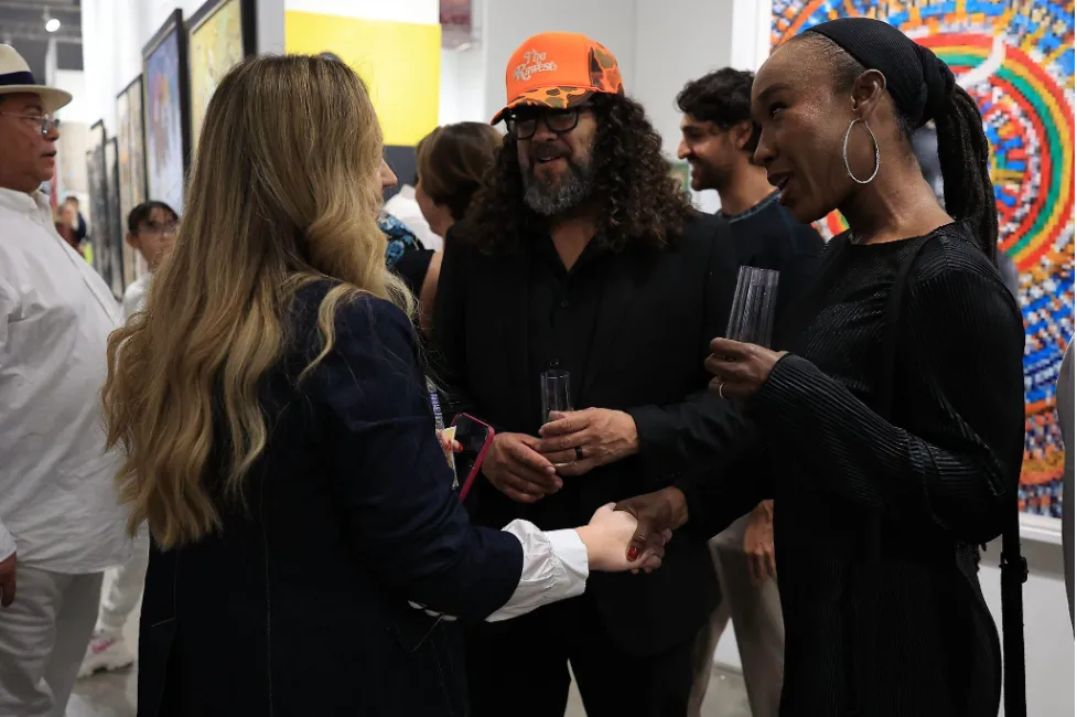 A candid moment at an art event where Venus Williams shakes hands with another woman, while two men stand nearby in a crowded gallery space.