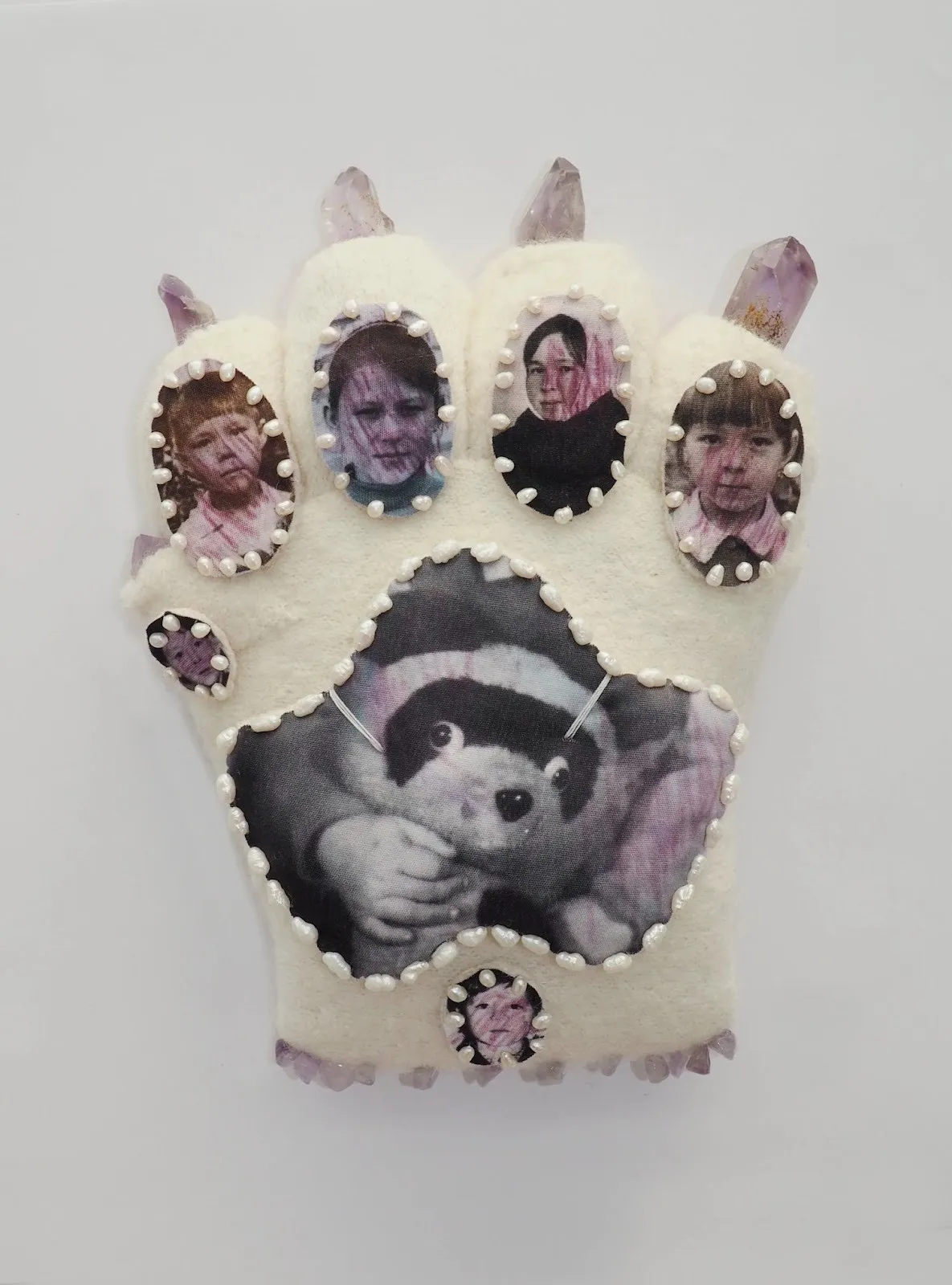 Glove-shaped textile artwork adorned with oval portrait images and pearls, with purple crystal points at each fingertip.