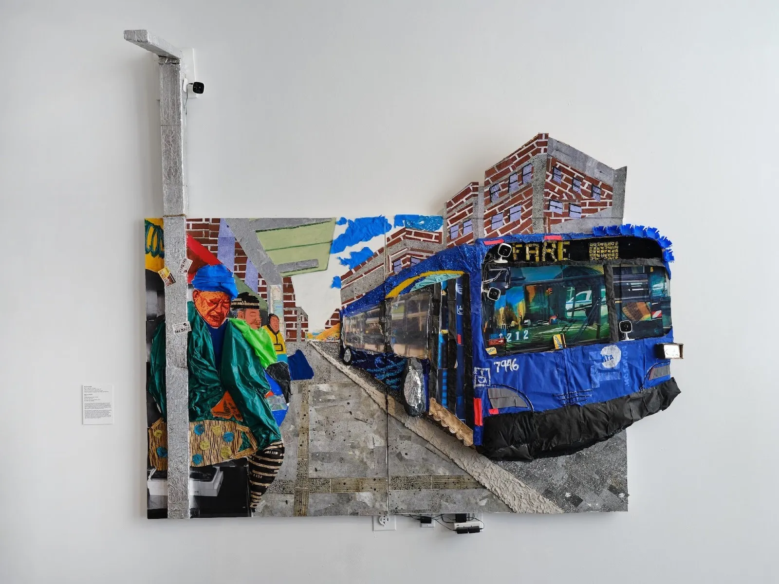Large mixed-media wall collage depicting a blue city bus and bundled figures against brick buildings and a street scene.
