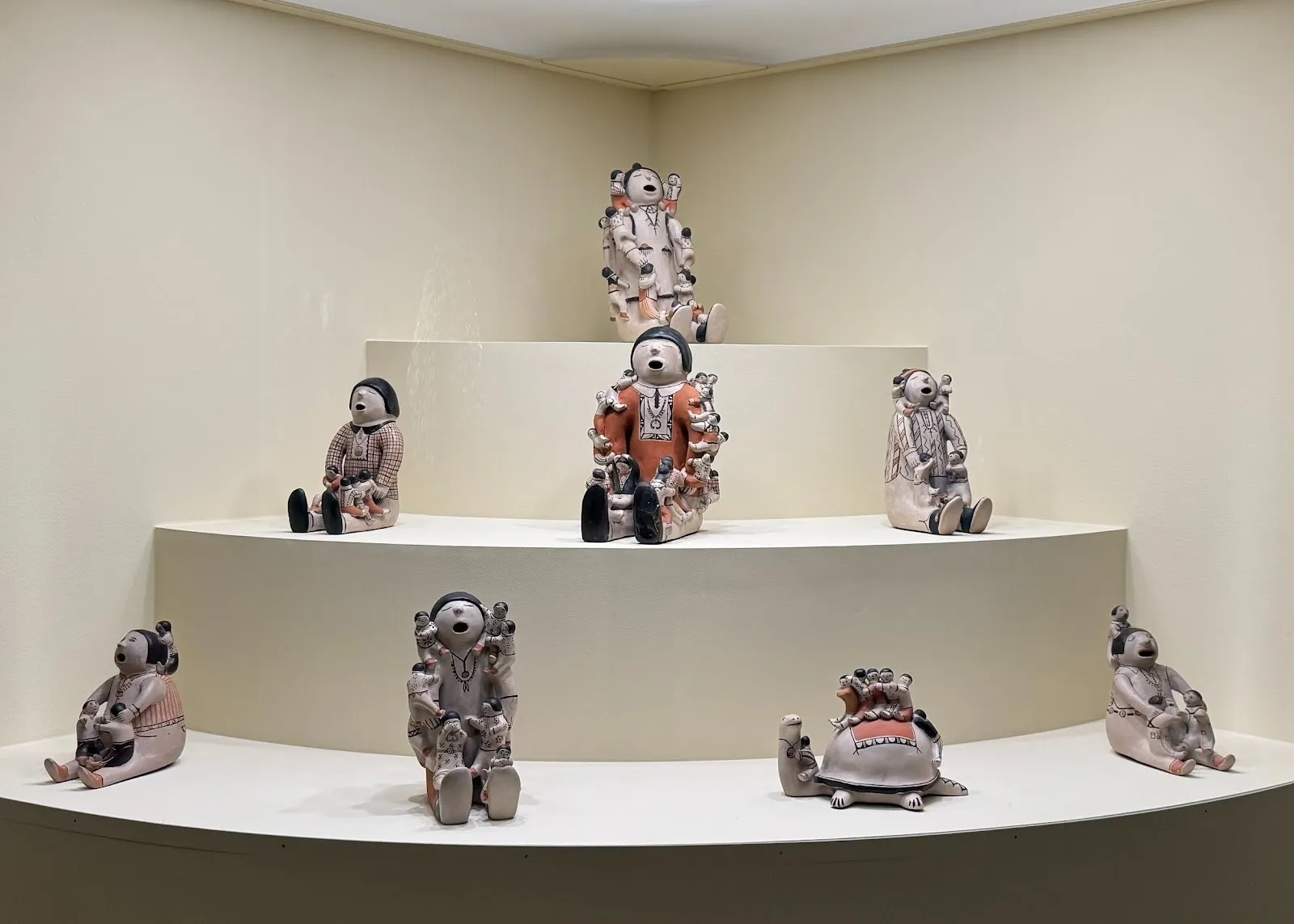 Tiered display of ceramic figures seated with open mouths, arranged in a curved wall niche.