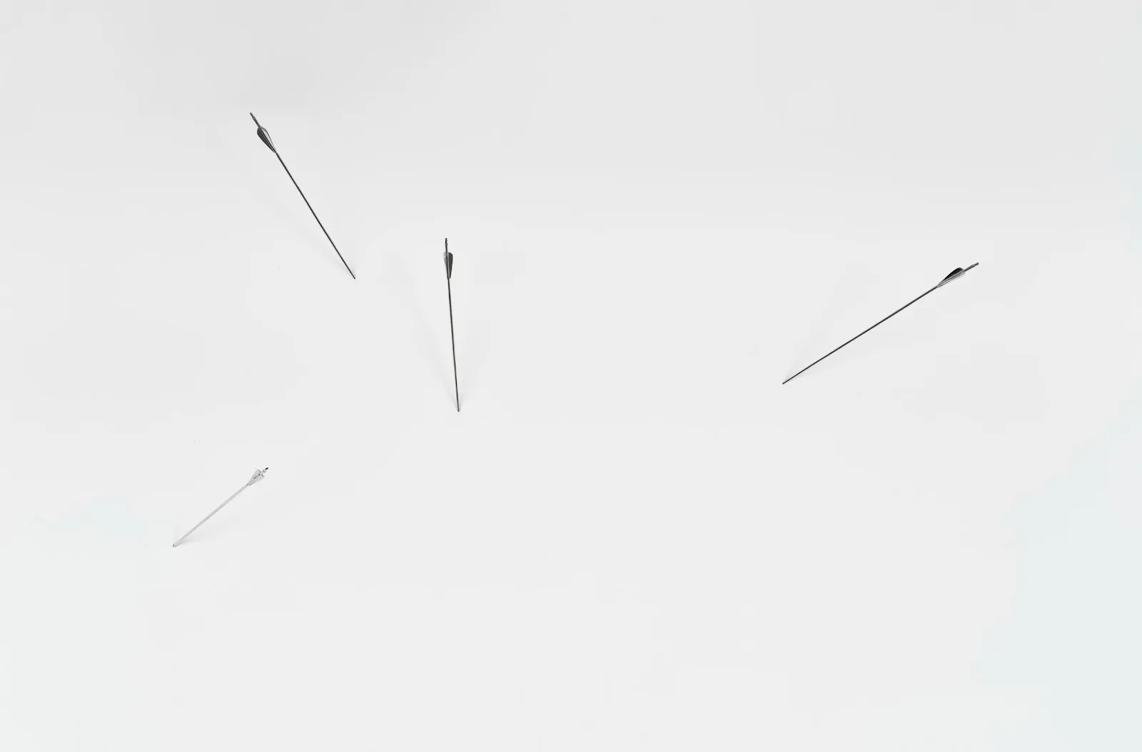 Four silver chrome arrows pierce and stick into a white wall at different angles.