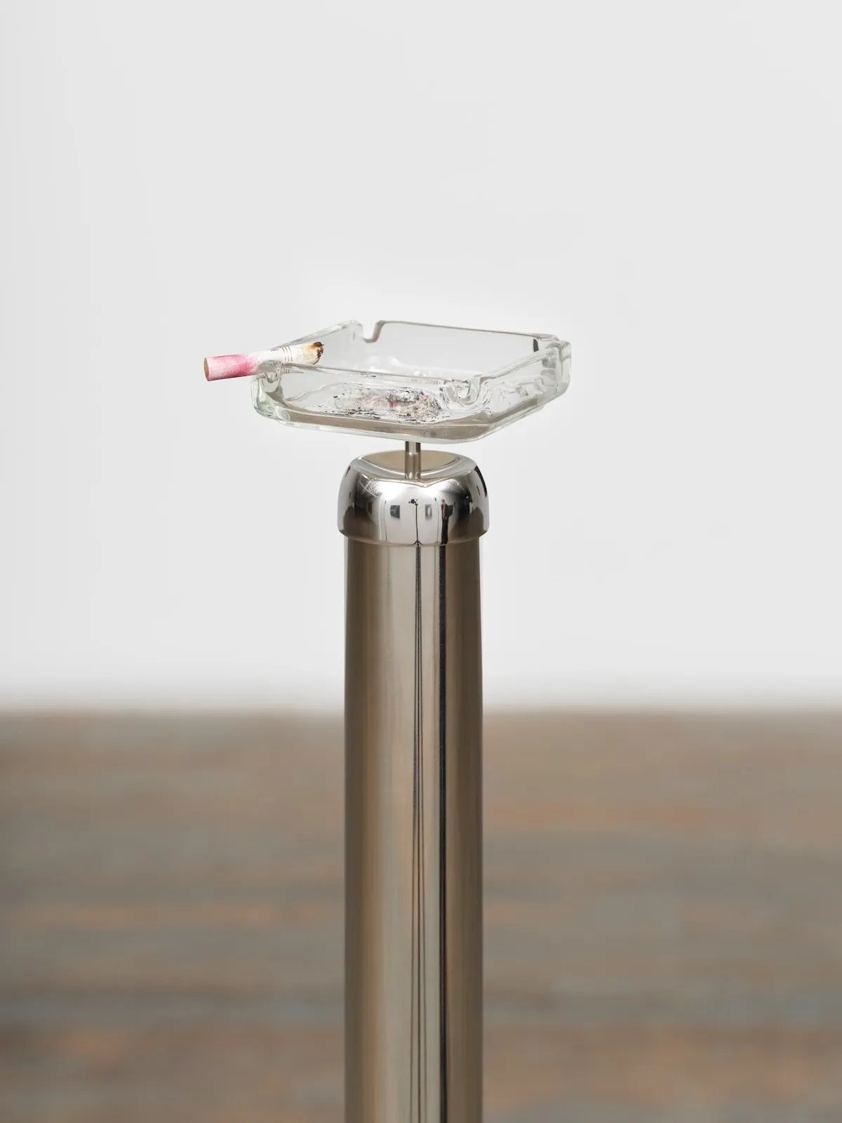 A glass ashtray with a lipstick-stained cigarette stub is affixed to a chrome silver post.