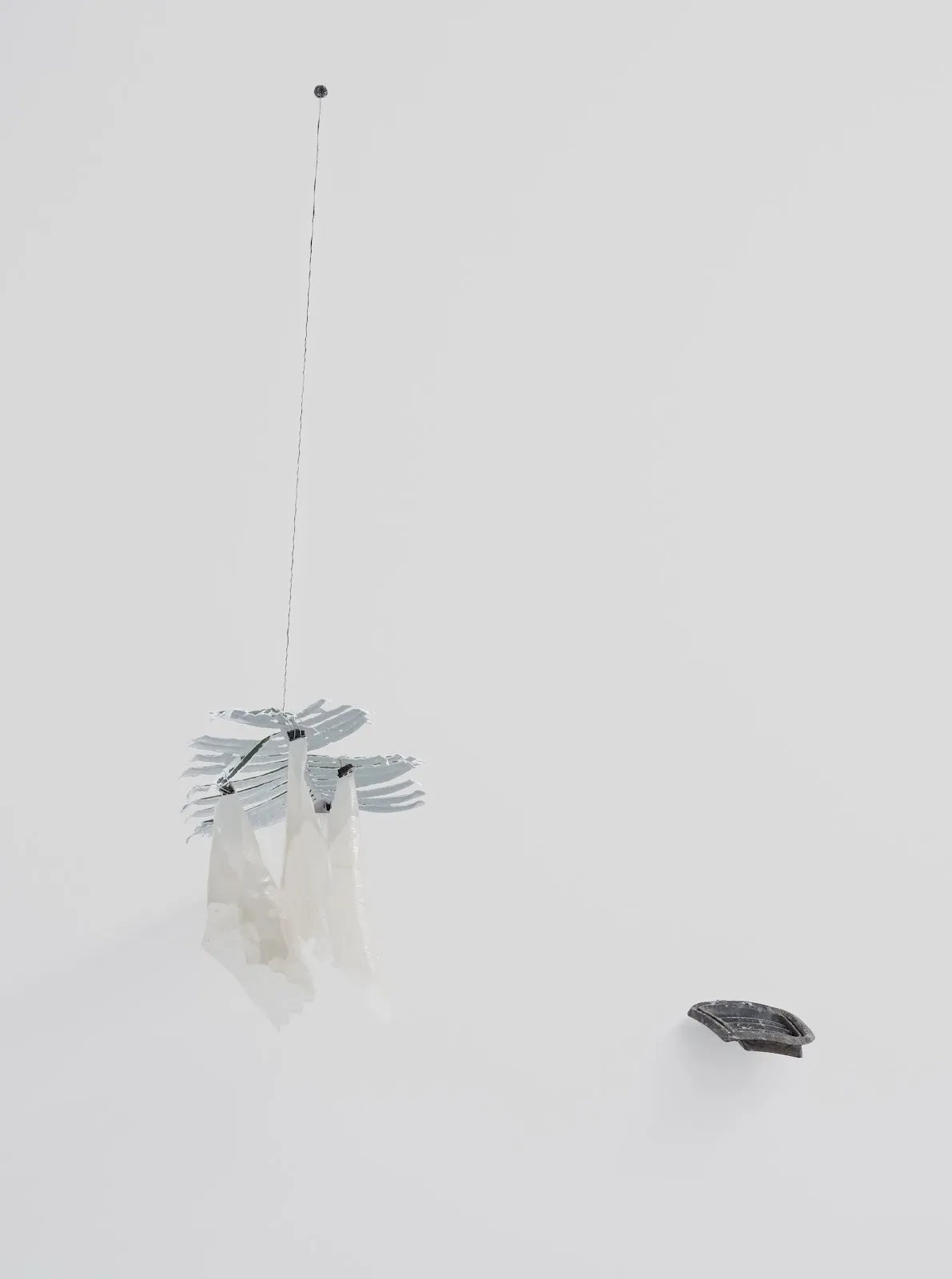 Hanging kinetic sculpture with pale leaf-like pieces and translucent material suspended from a thin wire.