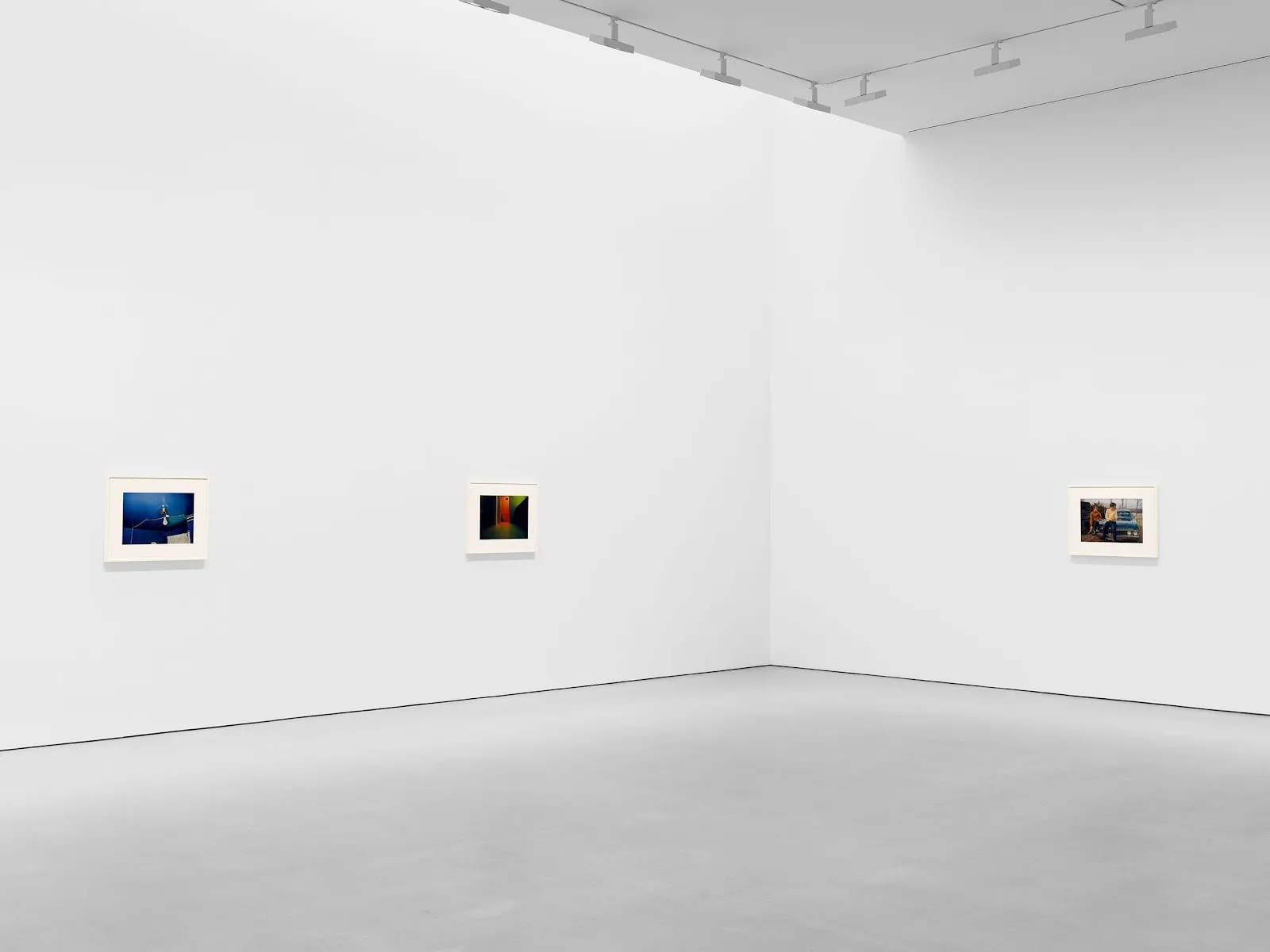Gallery installation view with three small framed photographs spaced across white walls.