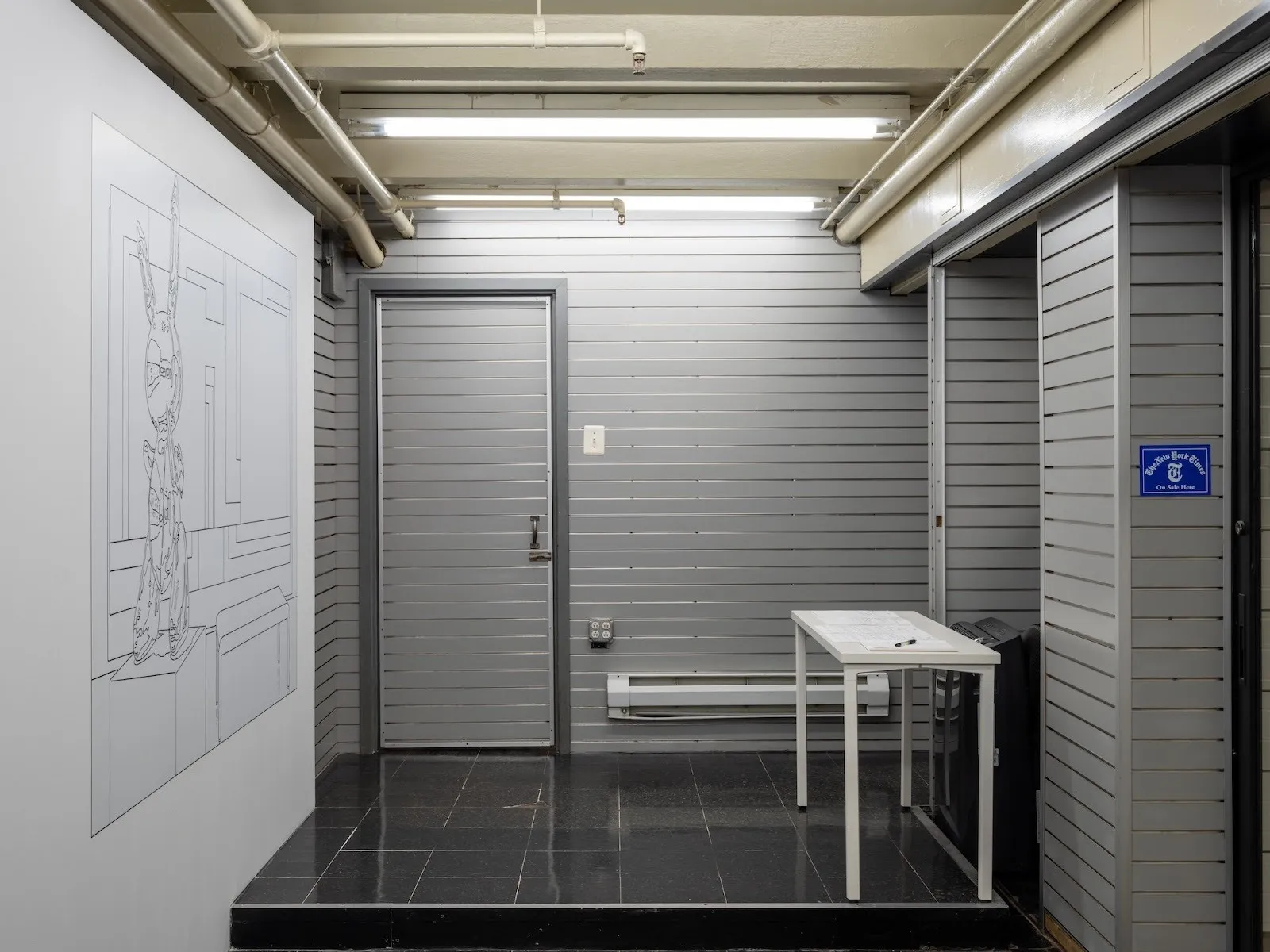 Interior gallery space showing a large wall drawing of a rabbit sculpture, with a white table and sign-in sheet nearby.