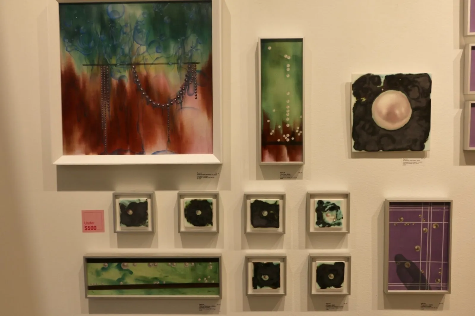 Gallery wall displaying colorful abstract paintings and small framed works, arranged salon-style.