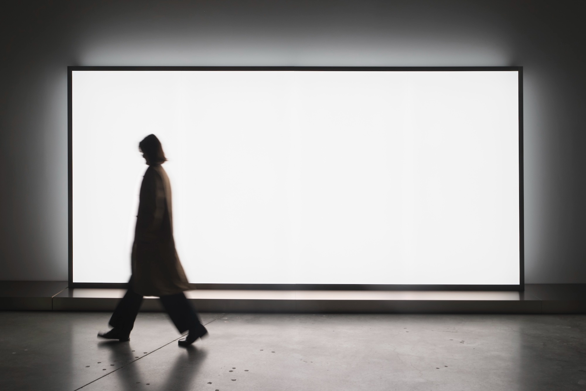 Silhouetted figure walking past a large illuminated white lightbox.