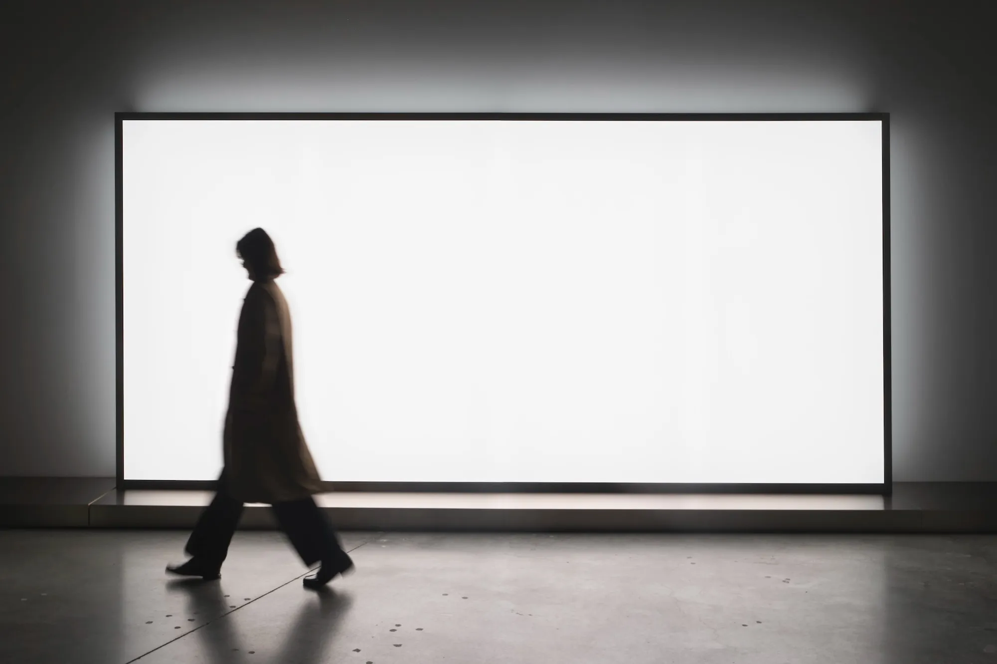 Silhouetted figure walking past a large illuminated white lightbox.