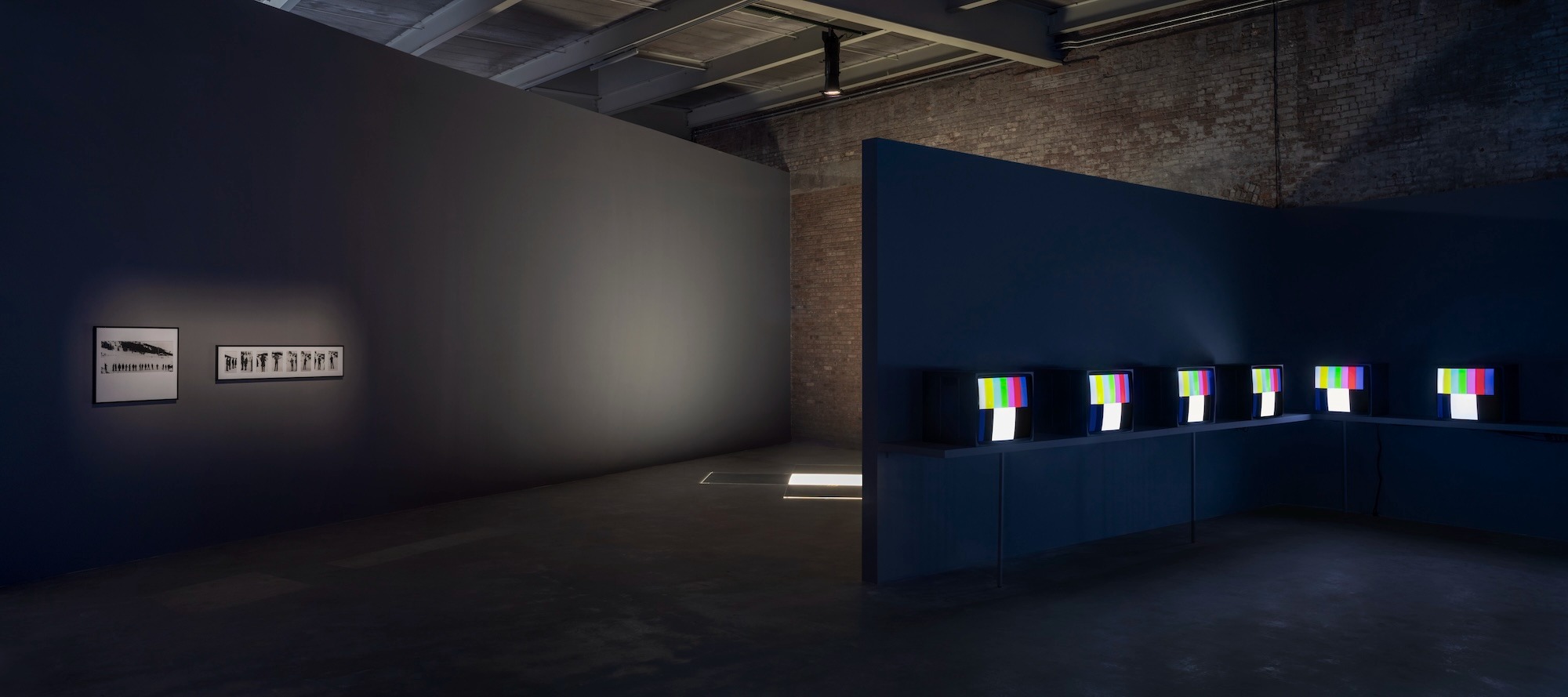 Dark gallery with CRT monitors showing color bars along a blue partition wall.