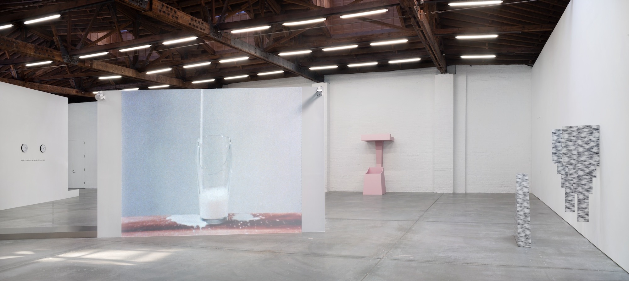 Projection of a glass filling with milk on a freestanding screen in open gallery.